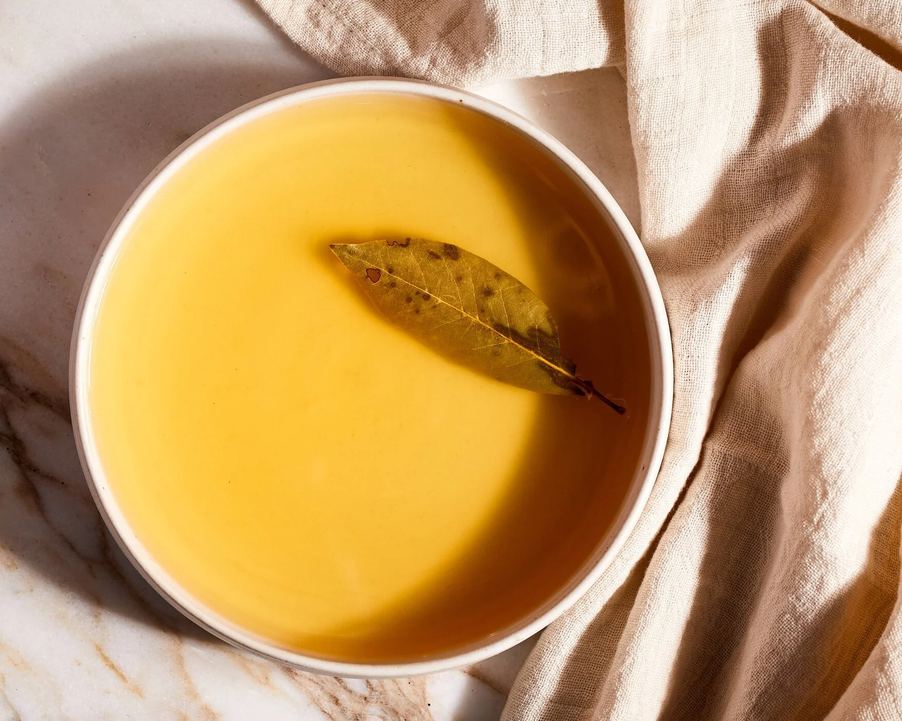 Golden organic chicken bone broth in bowl with bay leaf – nourishing and preservative-free
