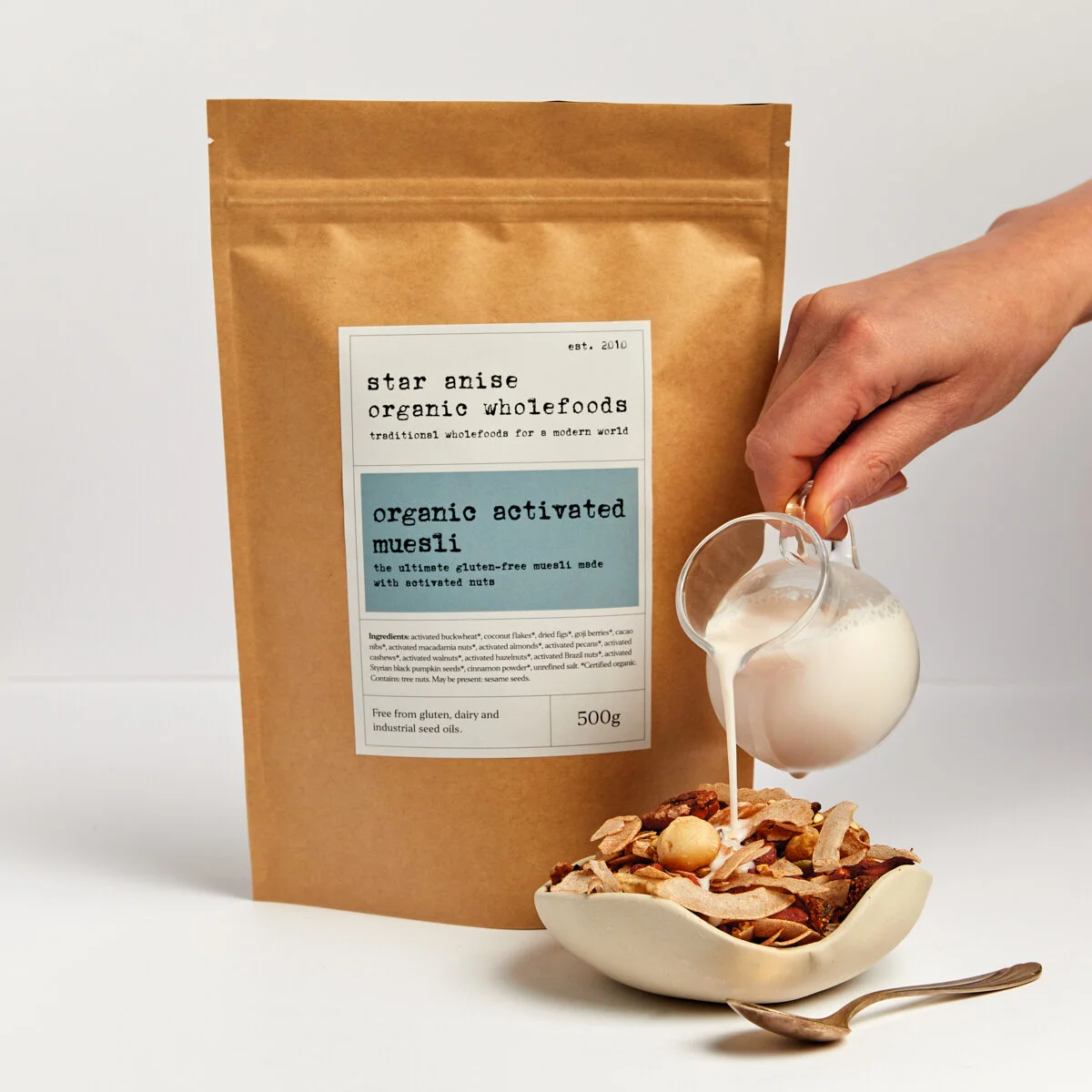 Organic activated muesli in a bowl with milk being poured, next to a 500g product bag