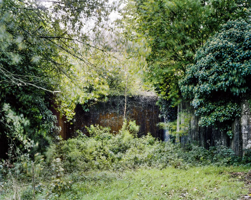 These are relics of a once vibrant chapter of Irish life. Like the dolmens John Montague crafted as a metaphor for the old people of his childhood, the ruins of these abandoned alleys bear silent testimony to a feature of Ireland that has perished through time and modernization. These plain walls were once the thriving open-air theatre's of their day. They were familiar meeting points, where people played games long into long summer evenings, and others gathered for simple companionship and discourse. The alleys came alive at a time in Ireland when human interaction needed little in the way of sophisticated props or accompaniments. In rural Ireland in particular handball captured the public imagination and societies grew around the games and the alleys which staged them. They became prized places of refuge, offering an escape from ordinary, hard-working lives. At the ball alleys, some strategically placed at crossroads in the open countryside, generations happily fraternized. Some were drawn by the magic and noise of a game which has deep Irish roots. But the alley was more than a sporting venue; it became a vital anchor for the community and an invaluable leisure outlet. It also served as an unofficial meeting point for lovers and revolutionaries. Even as a location for executions. It had an open charter - multiple, indiscriminate possibilities. Like Montague's dolmens, some alleys survive - a portion of them intact and a minority enjoying new leases of life. But the majority are disappearing slowly from the landscape to the point where they will eventually become extinct. Many have been merged and camouflaged into other structures, like farmyard sheds or car parks, so that they are barely recognizable or identifiable. Many others are simply abandoned and overgrown. Old handball players and the game's scattered aficionados will recall their last hurrah 50 odd years ago or more, after they had thrived across the country for over a century, before television and better transport began to signal their decline and offer alternative means of entertainment and social collusion - leaving each one in turn to become a tomb for a lost civilization.