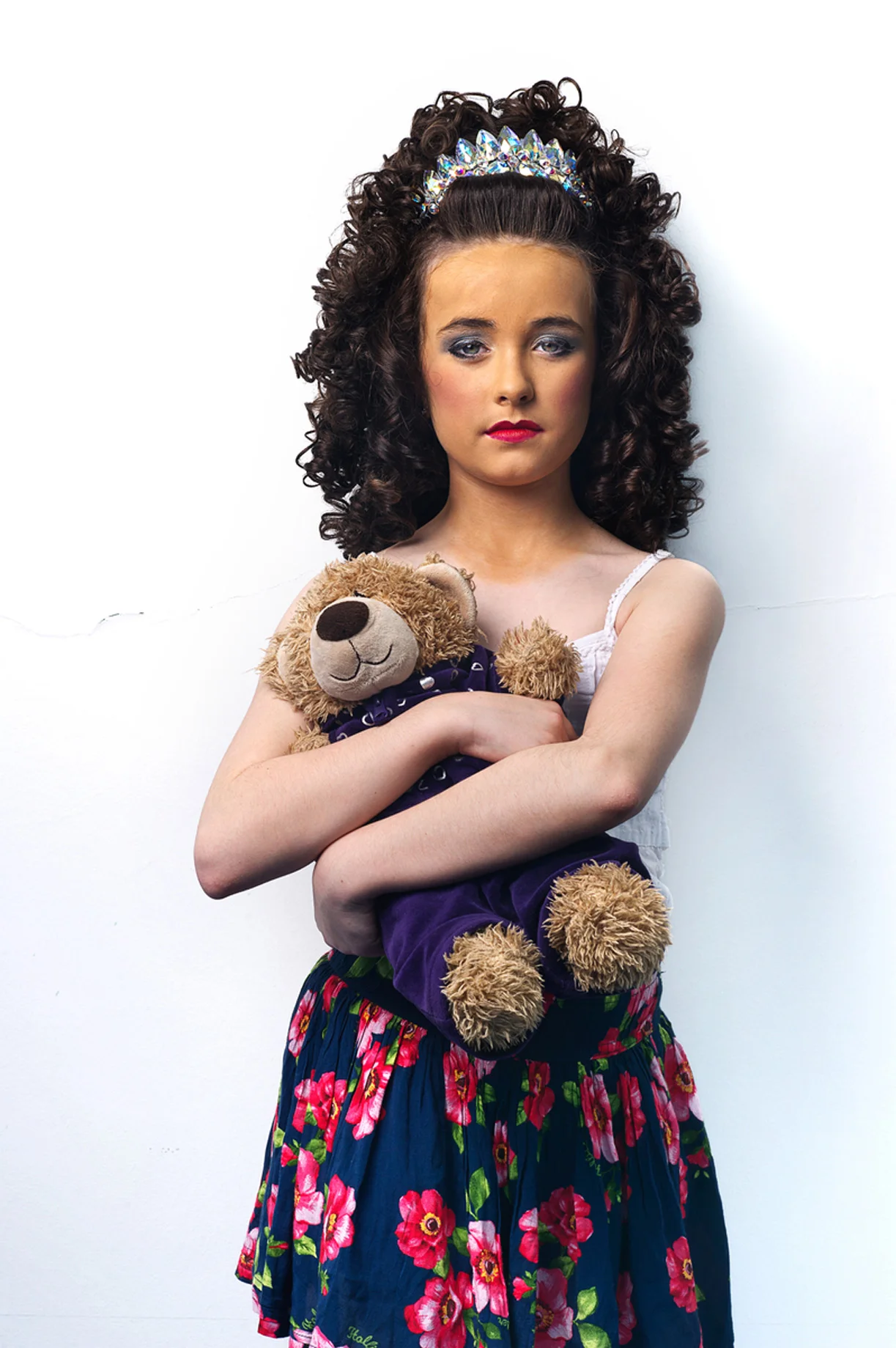 In 1994 during a seven-minute interval at the Eurovision Song Contest in Dublin a group of dancers took to the stage and proceeded to blow the audience away, including millions on television. Fronted by Michael Flatley and Jean Butler, soon to be household names, and accompanied by vibrant and relentless traditionalIrish music, this was the first public performance of the global phenomenon that would become known as Riverdance. Now fast forward to Belfast in April, 2012. Up to 4,500 competitors took part in the Irish World Dance Championships, an event that began in more humble circumstances in Dublin in 1970 – its aim being to promote Gaelic dance culture. Since then its popularity has gone through the roof with contestants travelling from all over the world to compete. The show is more than a dance discipline in the strict sense; the ‘look’ is also deemed important and almost an industry it itself. Contestants spray on fake-tan, carefully apply make up, attach wigs and tiaras and sport dresses that in some cases cost up to 4,000 Euro. It is an expensive environment as well as being a highly charged and extremely competitive one. Why do they spend so much time and money on costume? To catch the judges’ attention is the common explanation. Critics claim it is over-indulgent and garish and has little to do with the reason they are there – to dance, to promote culture. Advocates insist the dance is the most important facet on which contestants are scored and that irrespective of how ornate one’s embroidered dress, these choices are entirely discretionary. There are no hard rules governing dress sense. But it is widely accepted by those who compete and their families that unless you stand out visually then there is a danger you may be ignored. 