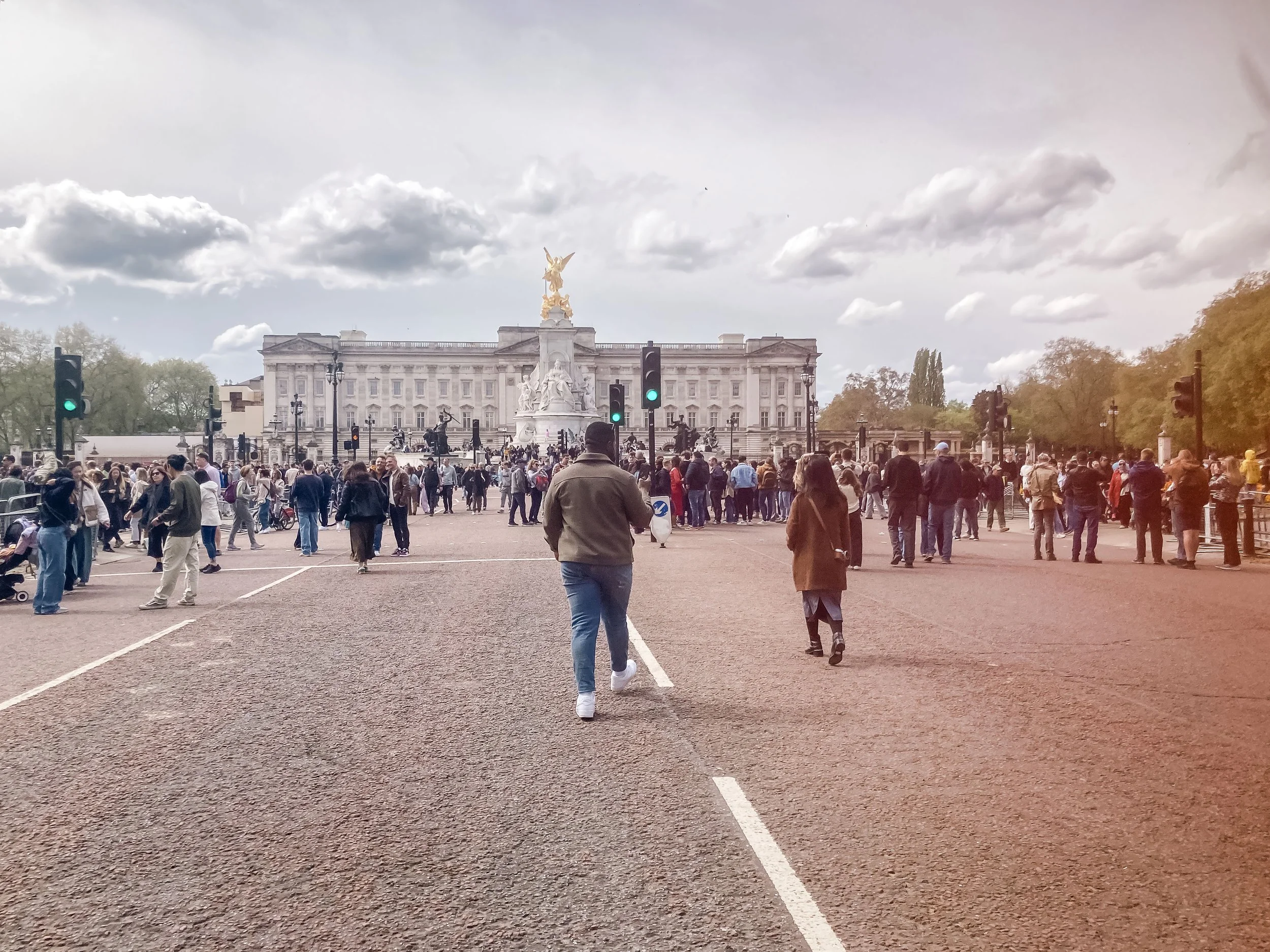Place occupée par de nombreuses personnes devant Buckingham Palace avec une statue dorée au sommet. Le ciel est nuageux.