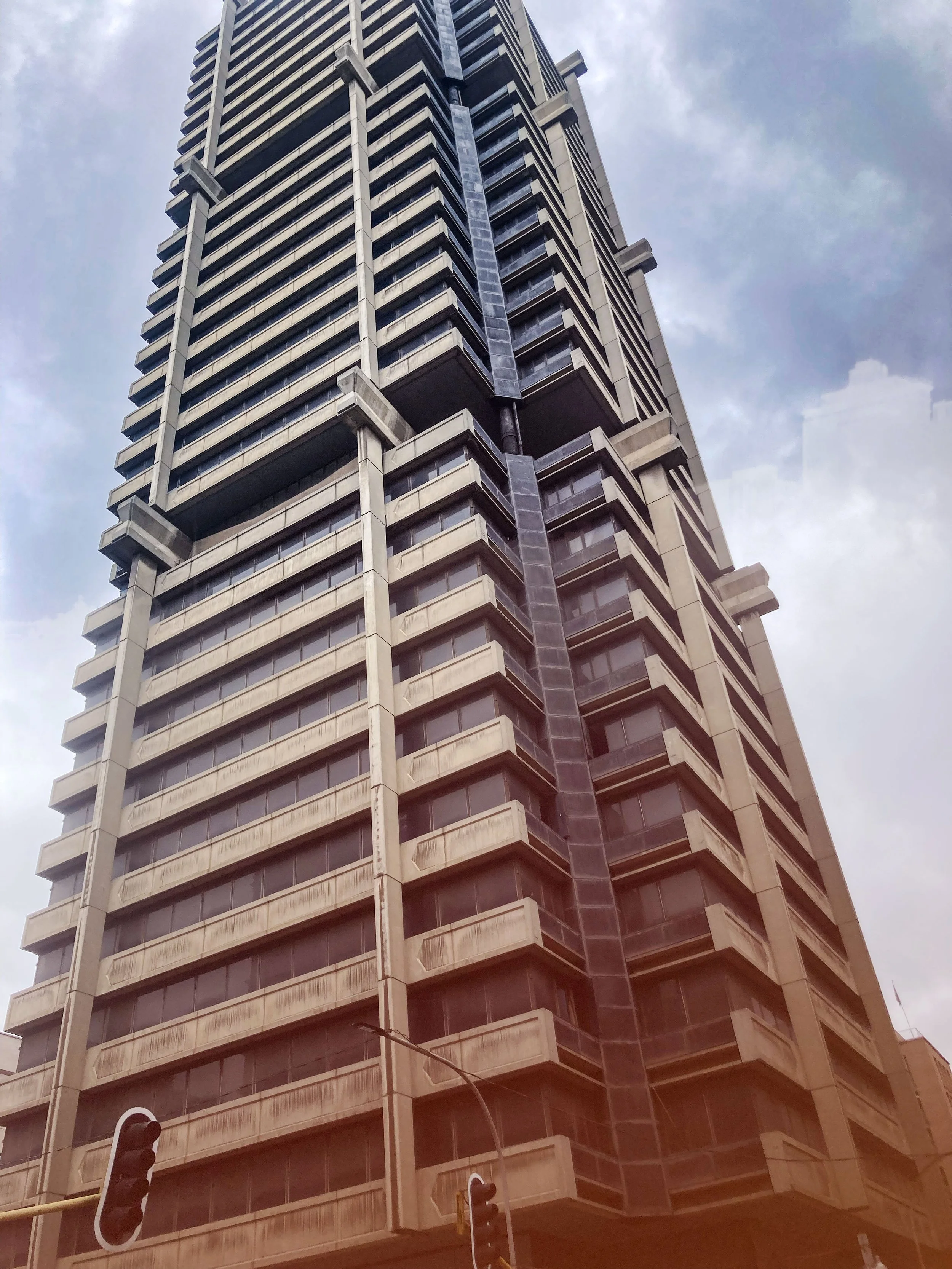 Une haute tour en béton avec de nombreuses fenêtres, vue de bas en haut, avec un ciel nuageux en arrière-plan.