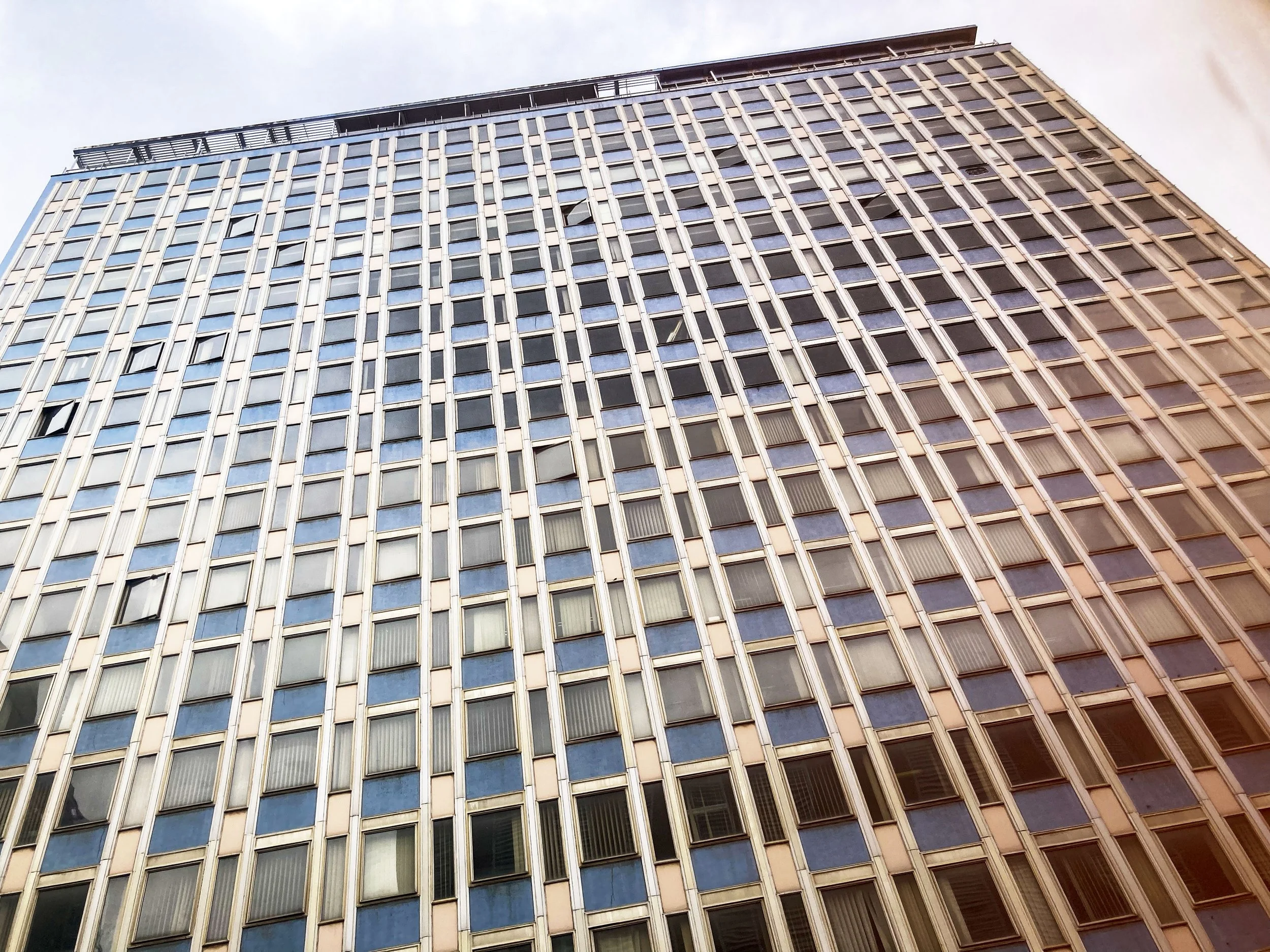Façade d'un grand immeuble de bureaux, vue de bas en haut, avec de nombreuses fenêtres en rangée.