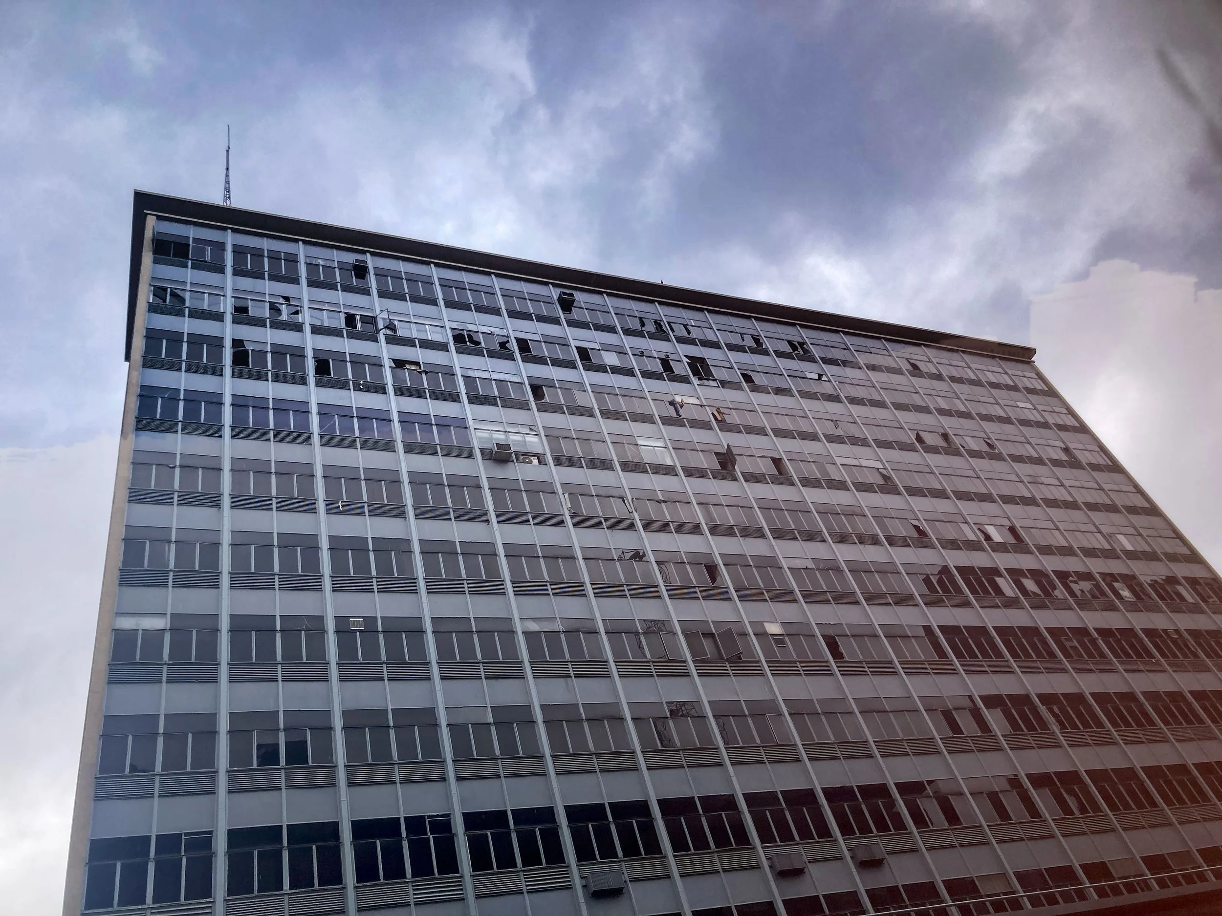 Une grande tour en verre avec de nombreuses fenêtres, vue de bas en haut, avec un ciel nuageux en arrière-plan.