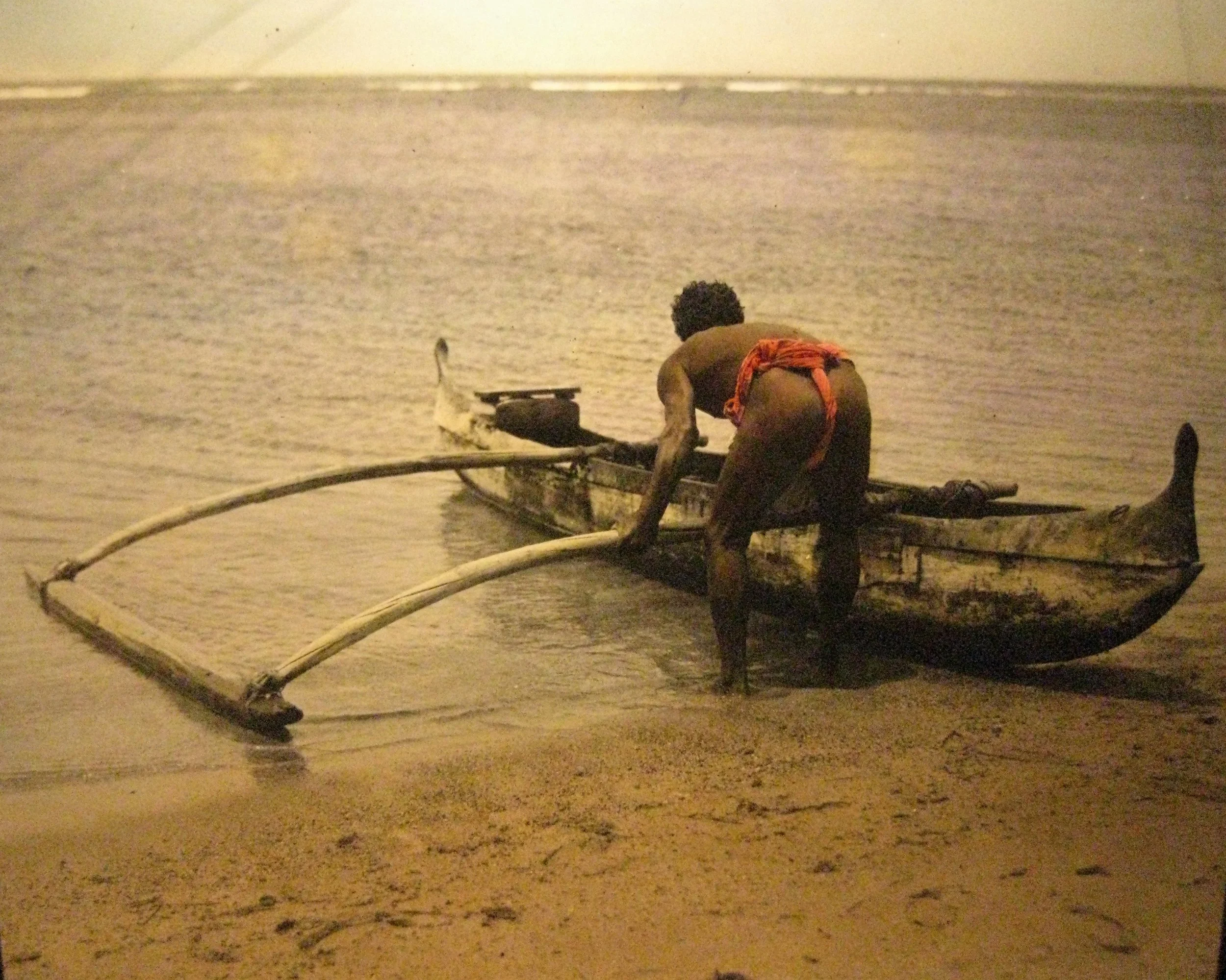  1913 magic lantern slide showing a Hawaiian pushing his outrigger to sea. 