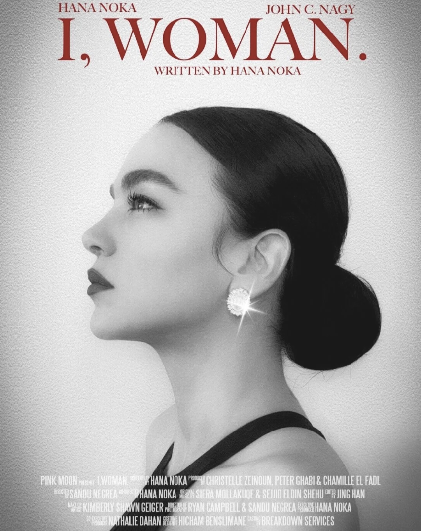Black-and-white promotional poster for the play "I, Woman" written by Hana Noka, featuring a profile image of a woman with dark hair in a bun, wearing a large earring, with text credits at the bottom.