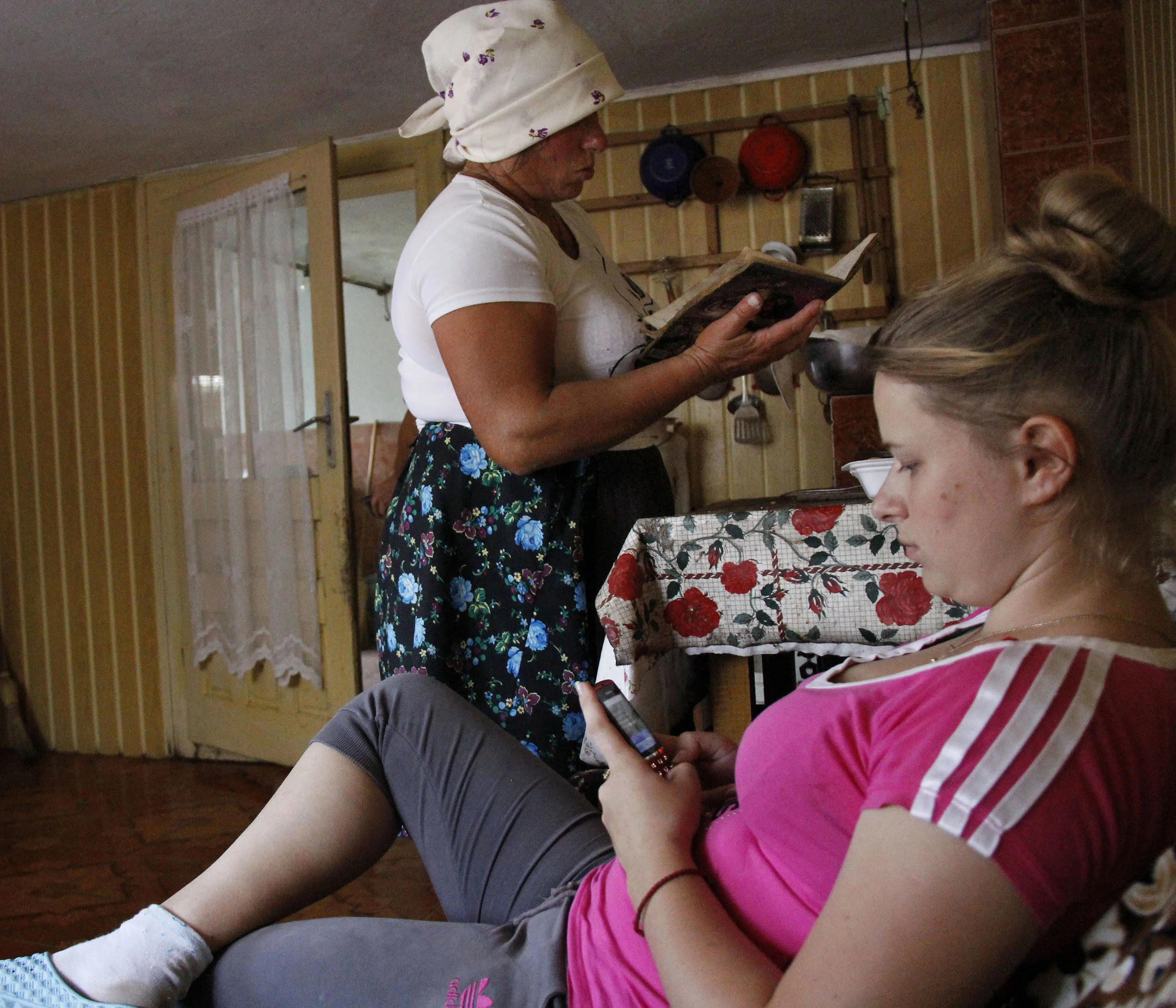  Marii sits in the kitchen texting on her cellphone while her mother, Viorica, makes dinner for St. Peter's Day on June 29. Families often spend an entire day preparing for the next day's holiday. 