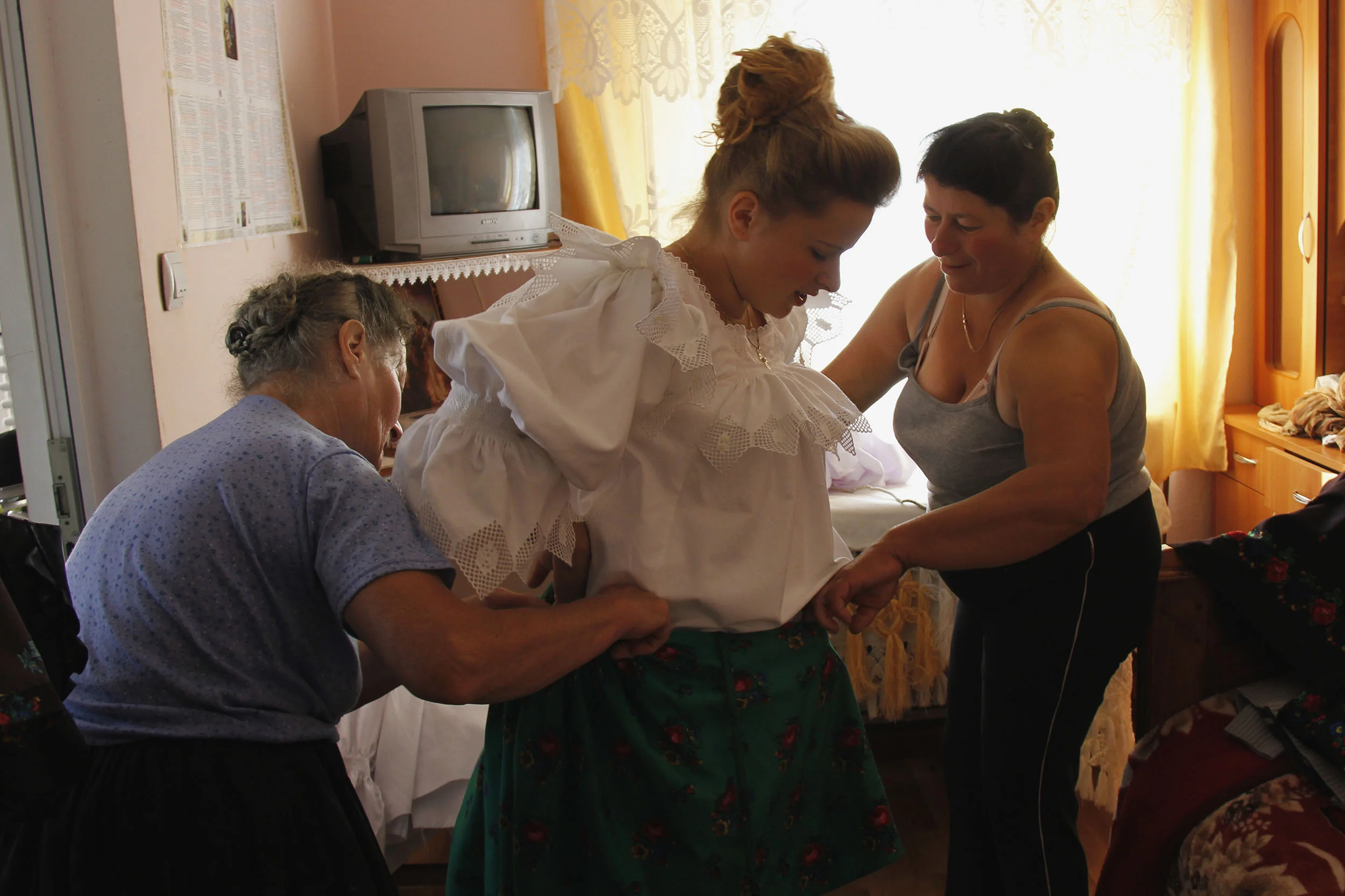  Viorica and Iliana help Marii dress in traditional clothing for church in celebration of St. Peter. On special occasions, village women and girls wear the traditional starched white cotton blouse trimmed in lace in addition to the traditional flower