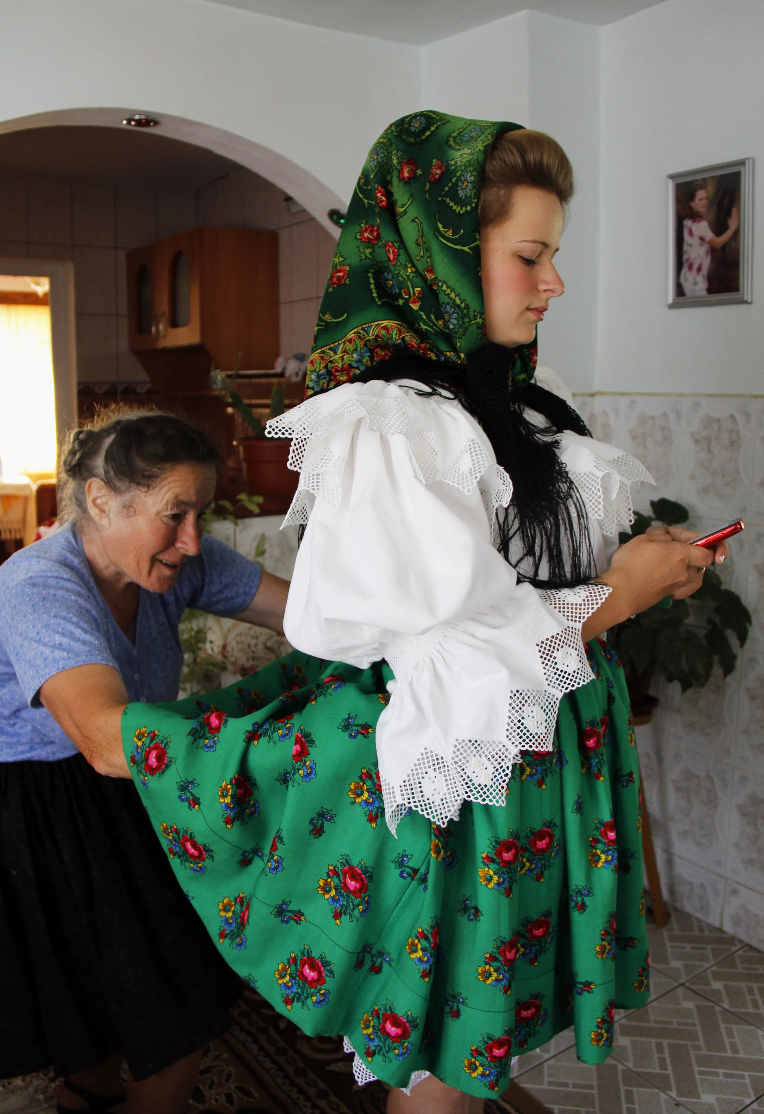 Marii's grandmother, Illiana, helps her add the finishing touches to her skirt before they leave for the St. Peter's Day parade and mass on June 29, 2014. Marii would not be able to have her cell phone with her the rest of the day due do her traditional clothing not having any pockets, and texted with her friends to coordinate where they would meet at the church.