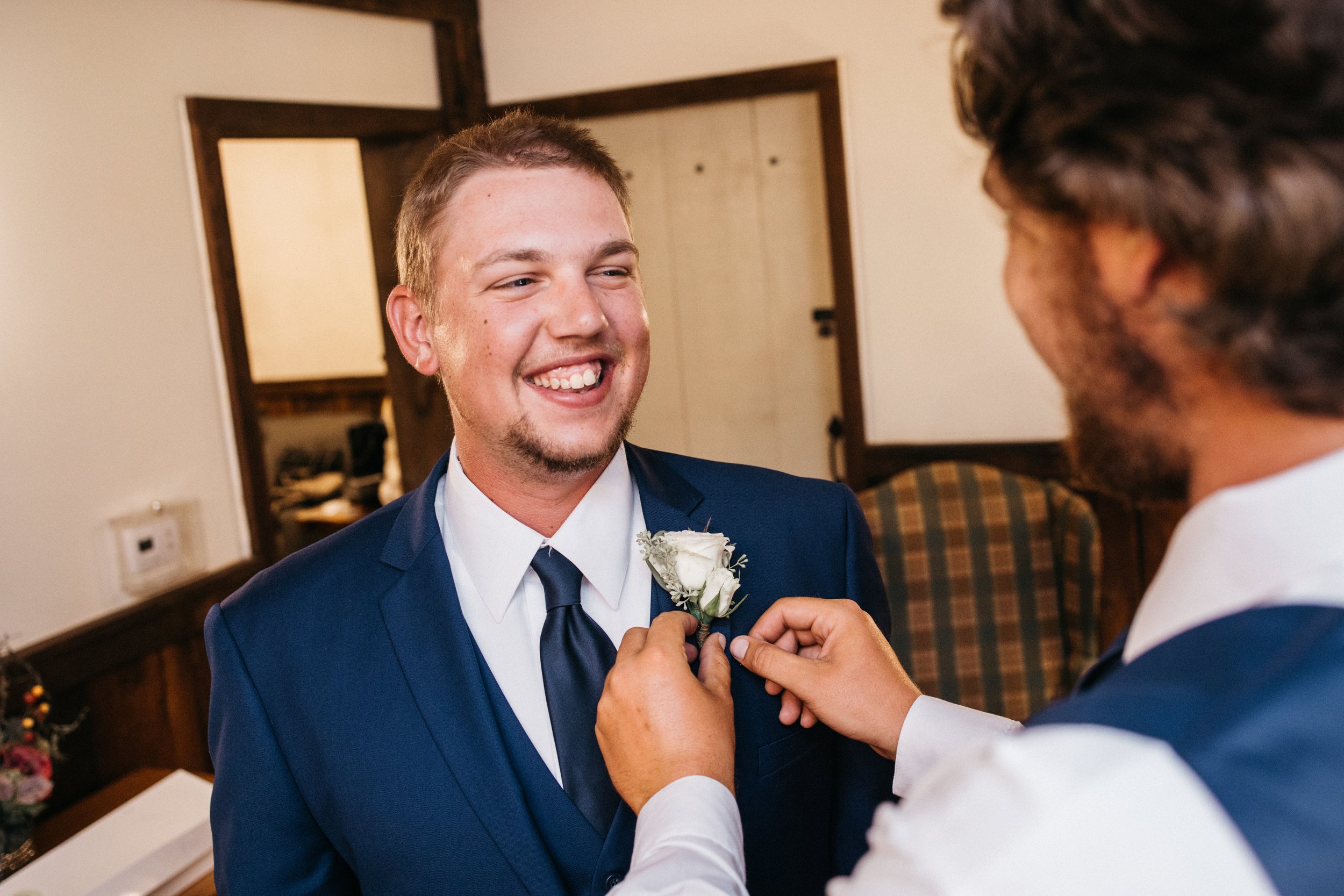 A groomsmen puts a white rose boutonniere on a groom.