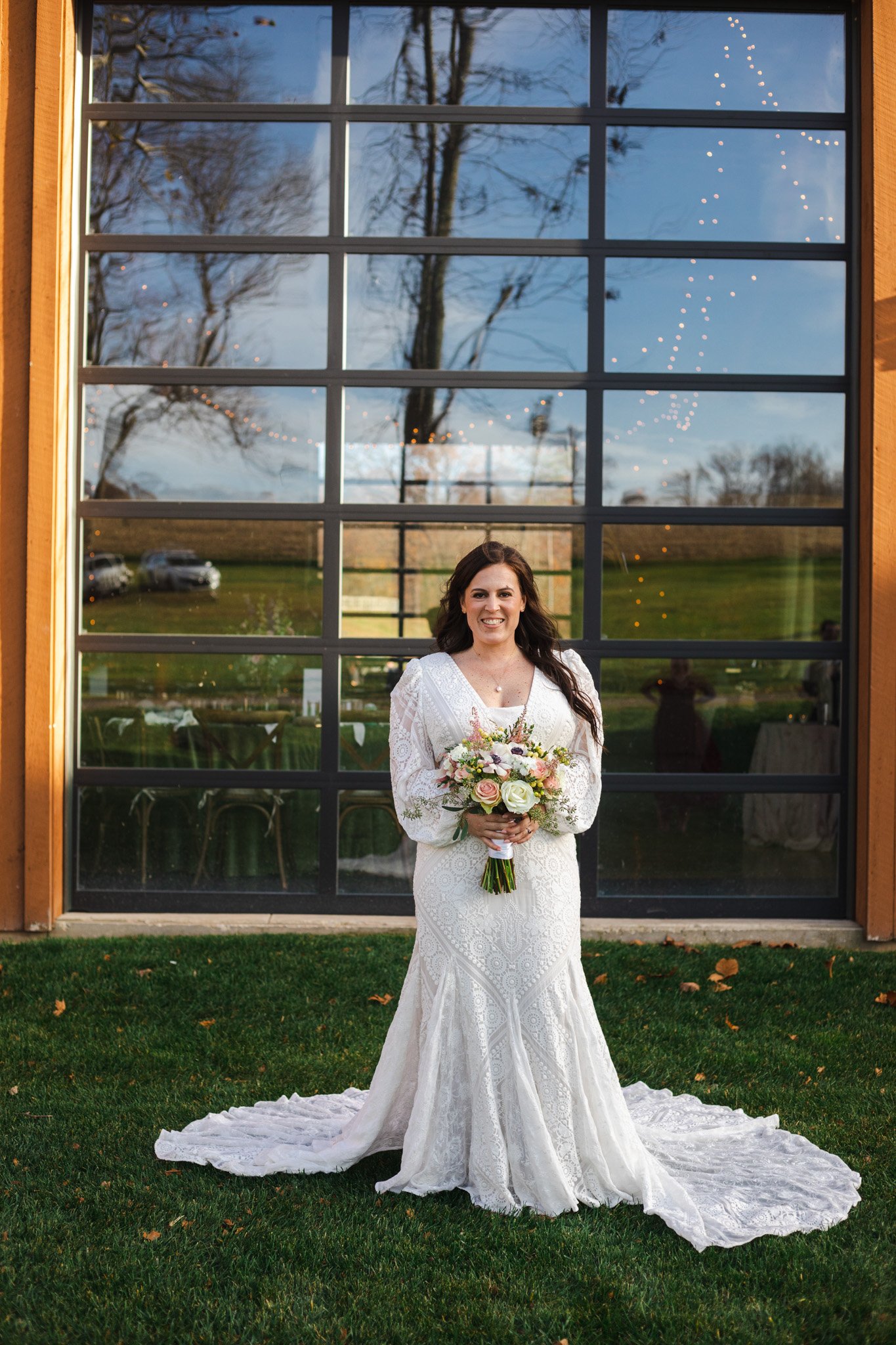 A bride standing in front of a window holding her boquet.
