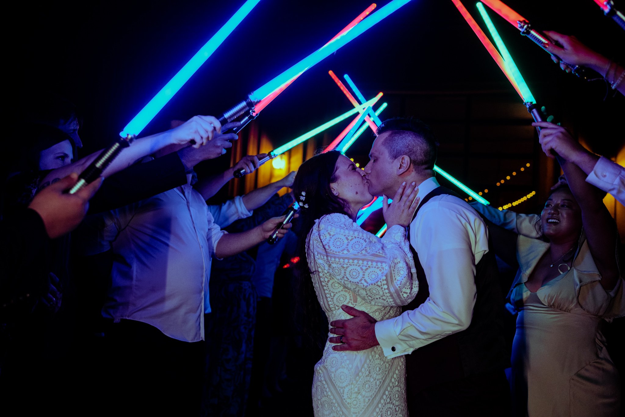 A bride and groom kiss under a light saber send off on their wedding day.