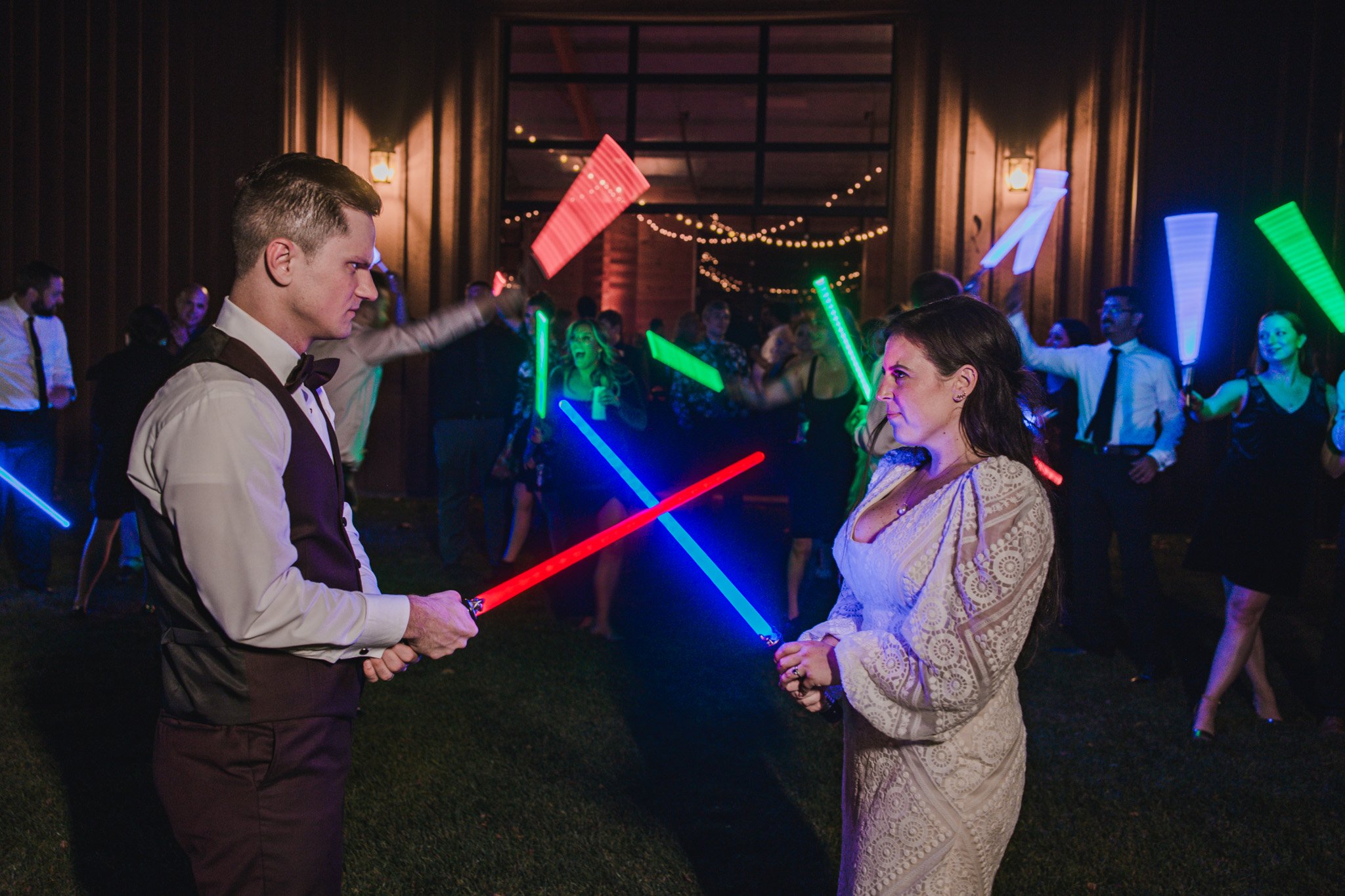 A bride and groom with light sabers, making a fierce face.