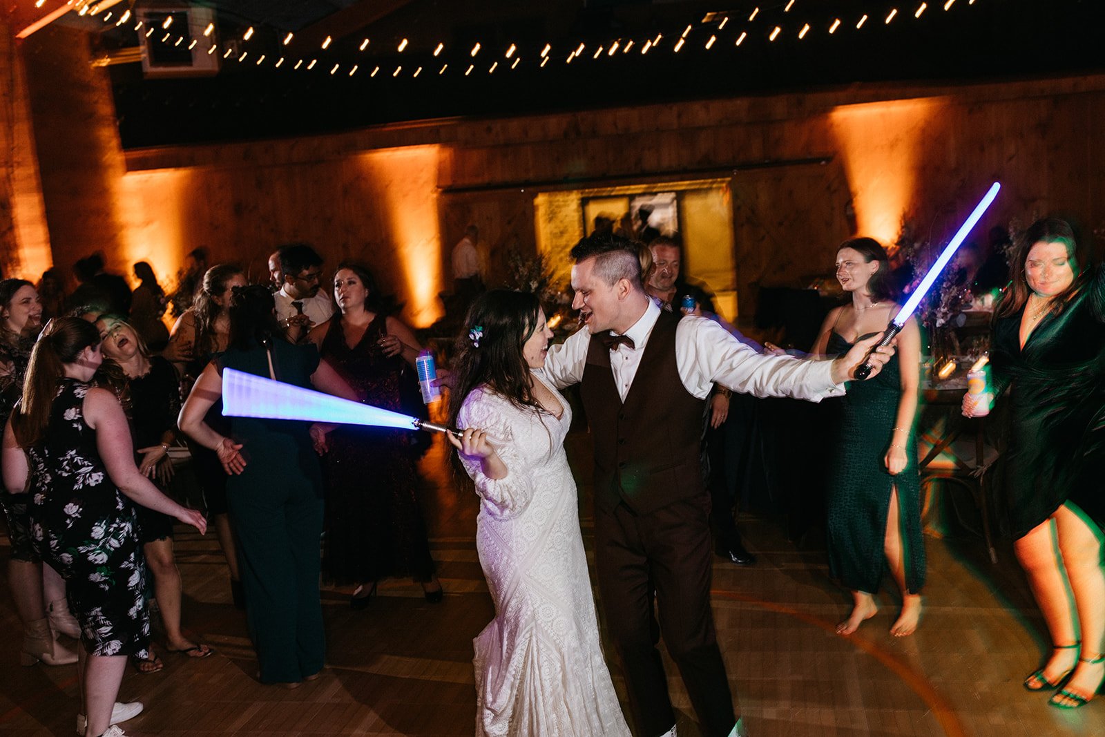 A bride and groom with lightsabers at their wedding reception.