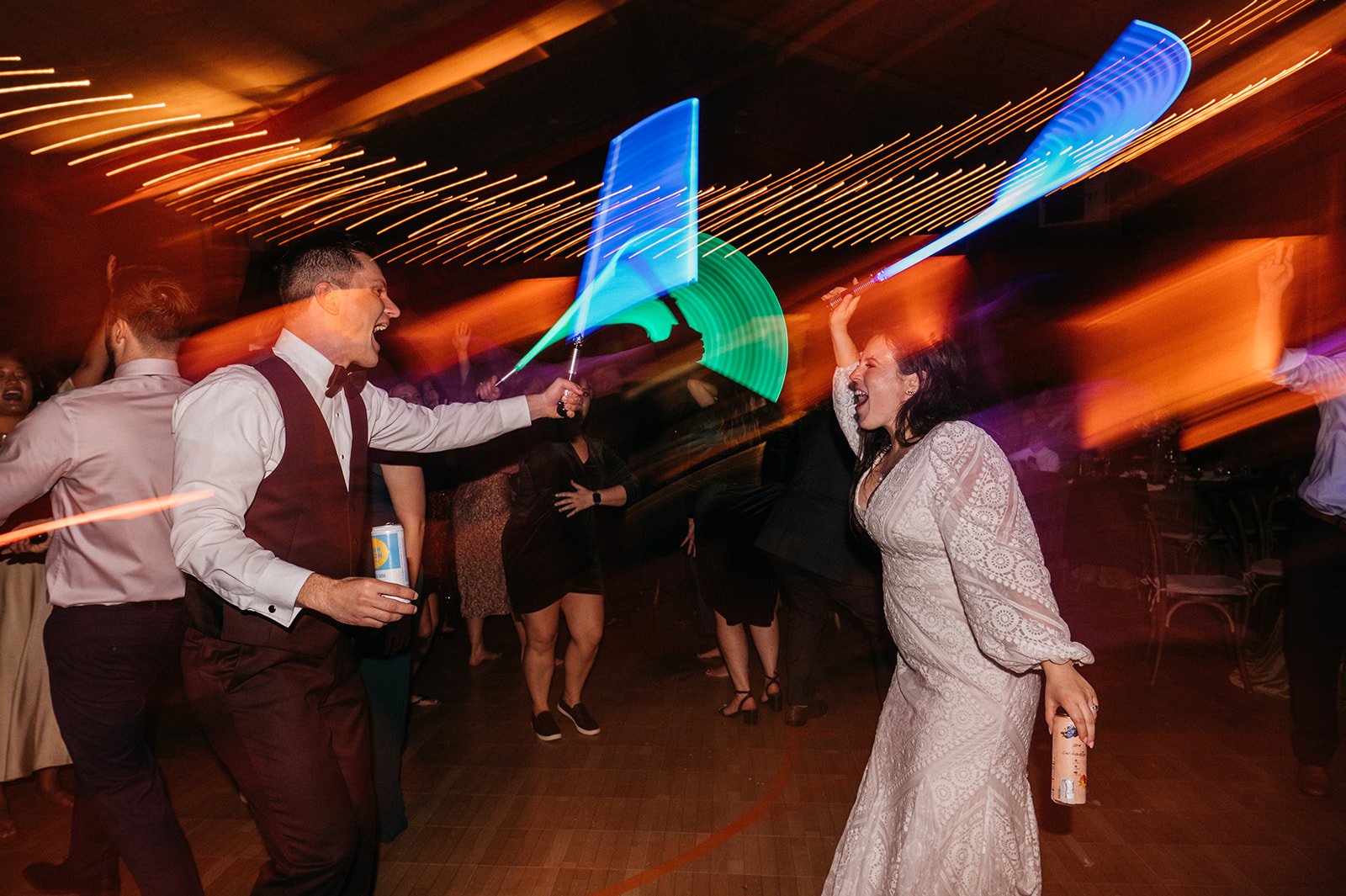 A bride and groom at their wedding reception dancing with light sabers.
