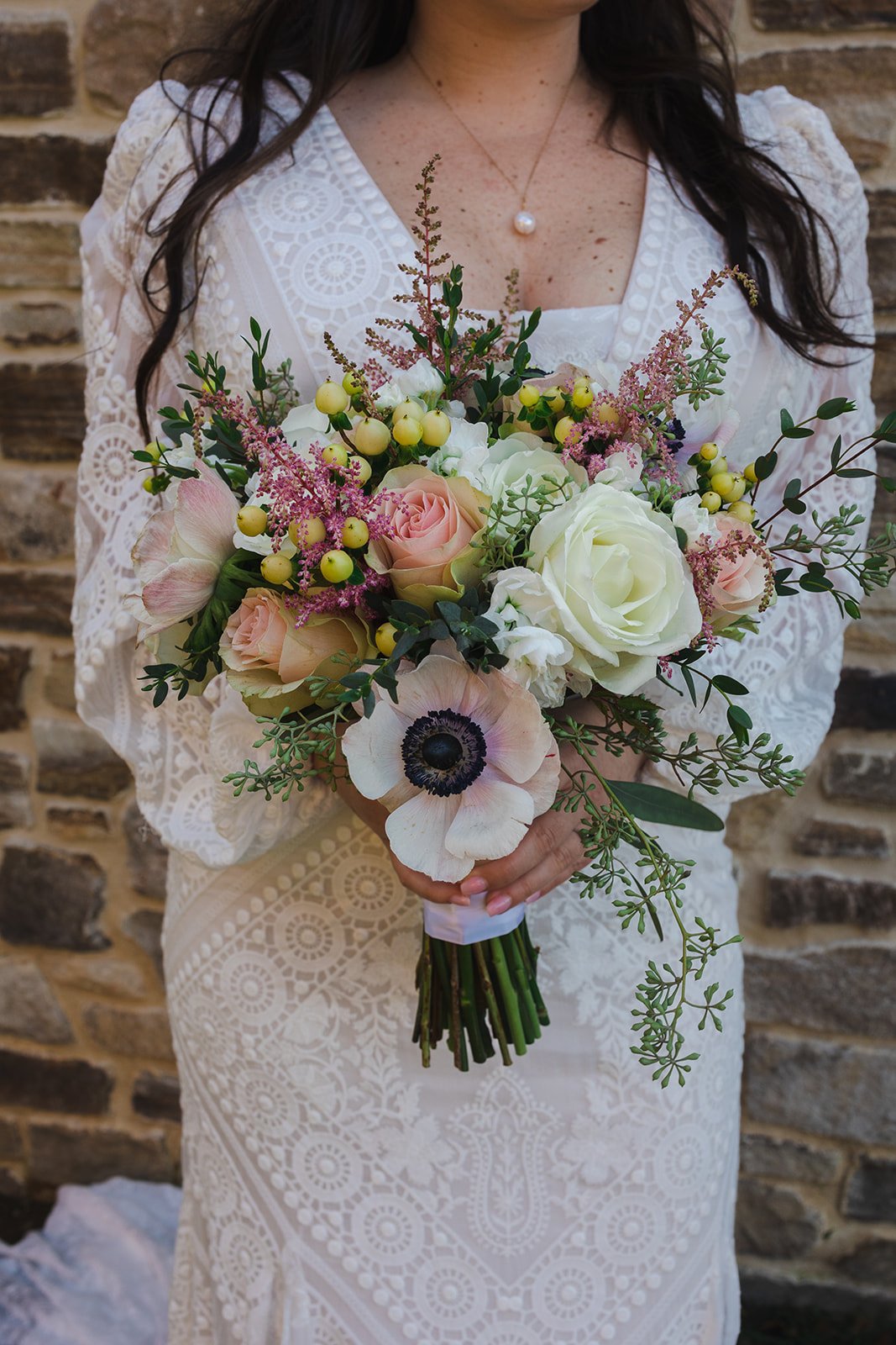 A bride with a wedding bouquet of blowers include a white rose and anemone. 