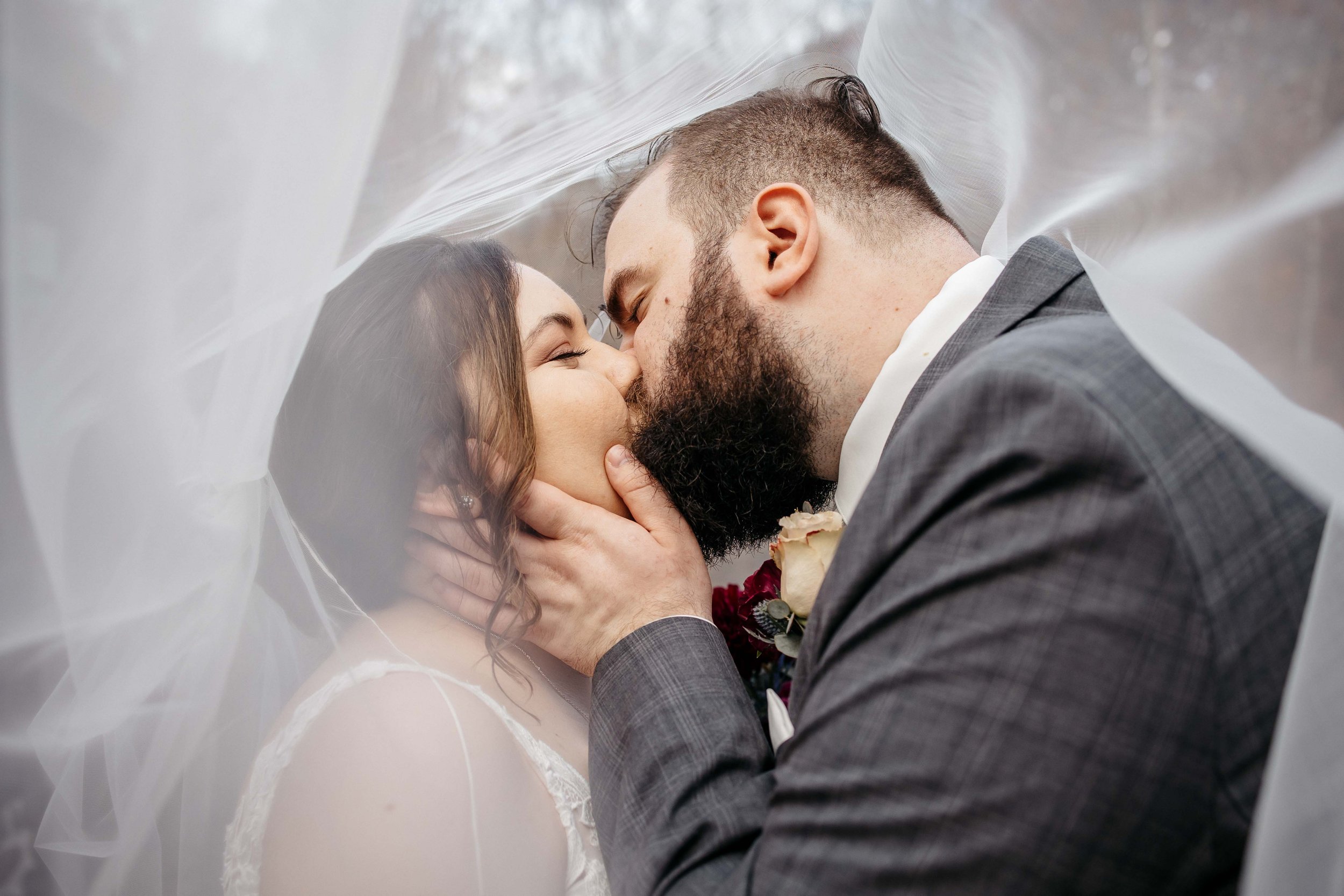 A bride and groom kiss under a cathedral veil.