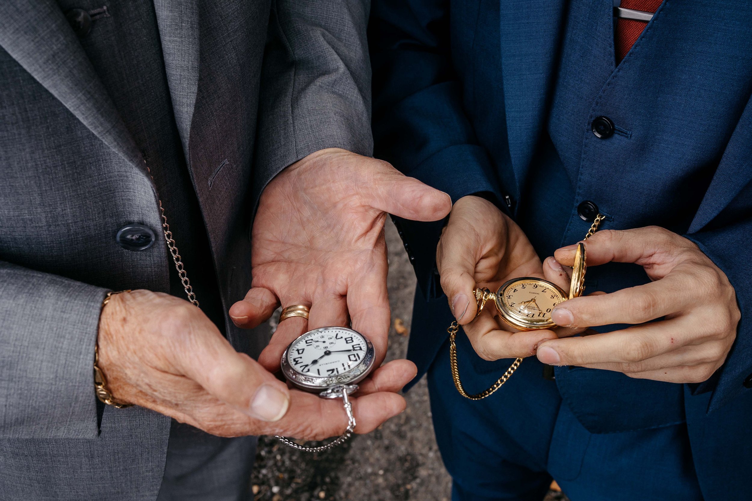 A groom and his father holding pocket watches.