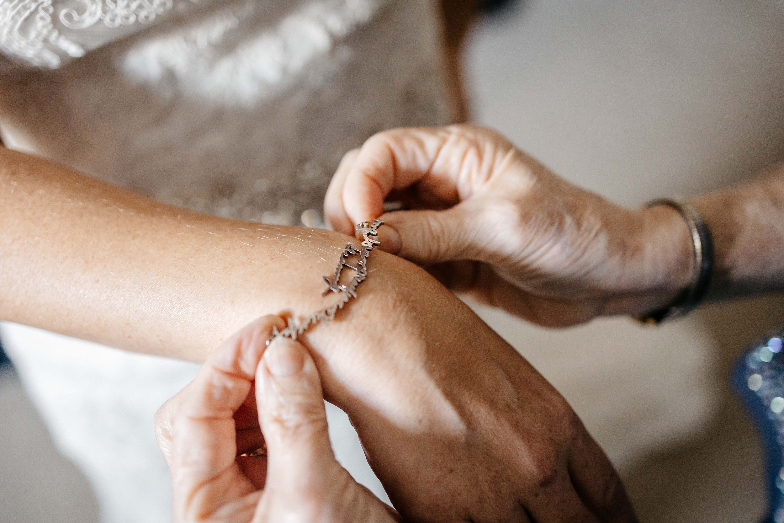 A mom puts a bracelet on a brides hand.