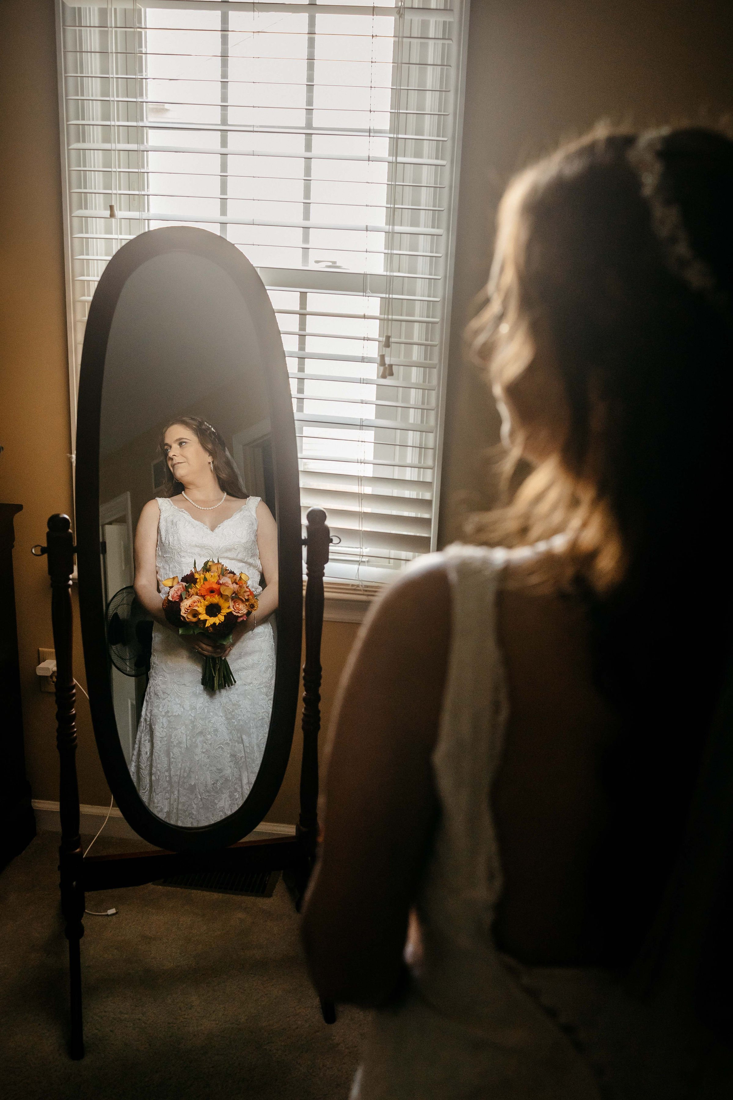 A bride looks into a tall mirror.