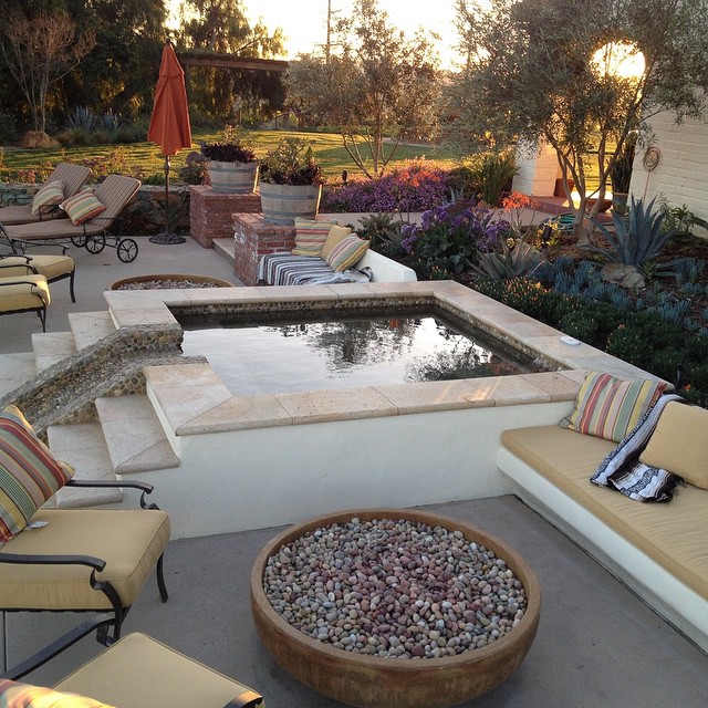 Detached spa with small pebble spillway and built-in seating benches.