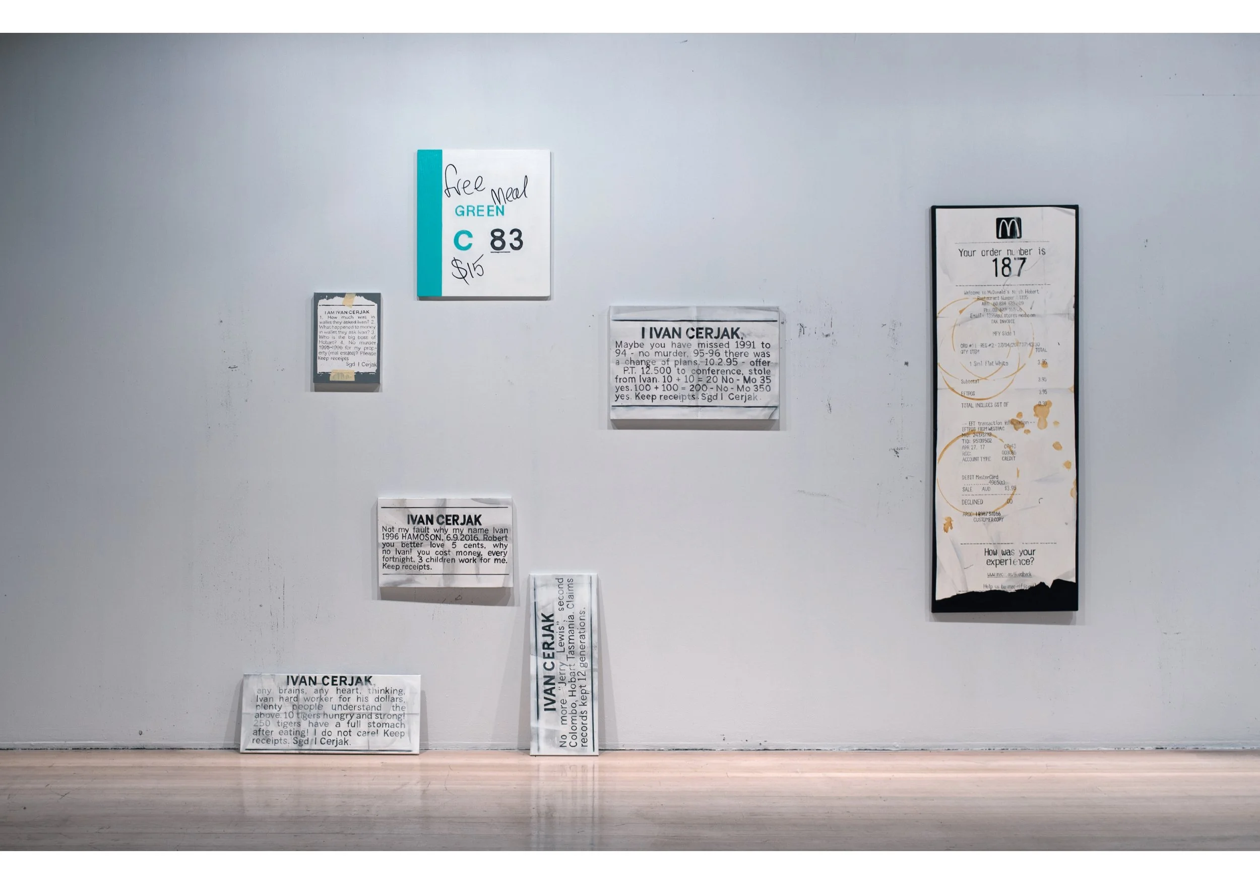 paintings of Several handwritten and typed notes and receipts taped to a white wall, with some overlapping and placed at different heights, next to a wooden floor.
