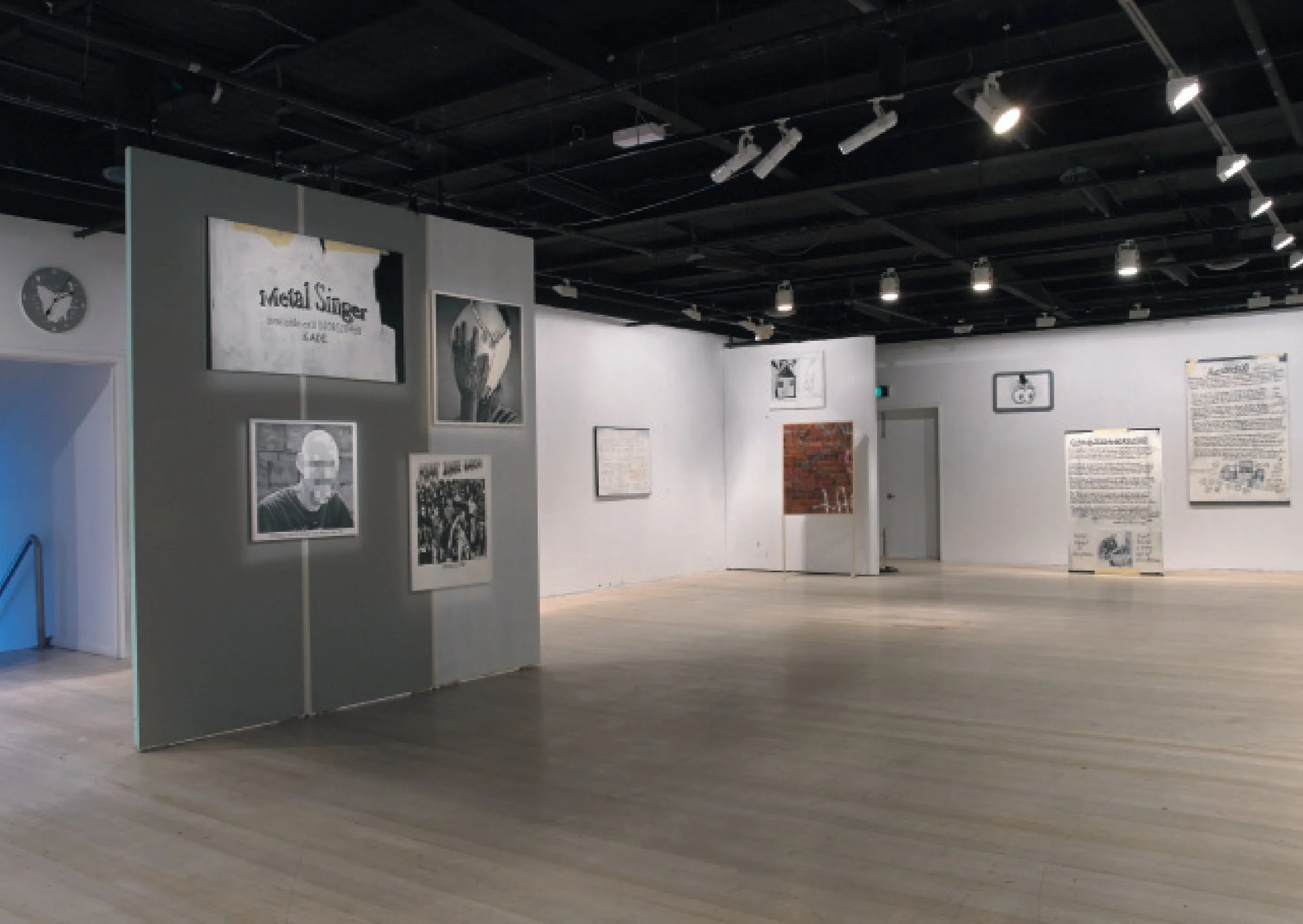 An art gallery with framed black and white photographs and text-based artwork on white walls, wooden flooring, and overhead track lighting.