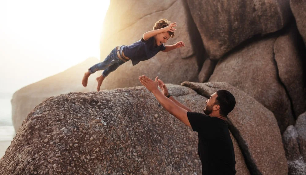 trust - father catching son jumping off a rock