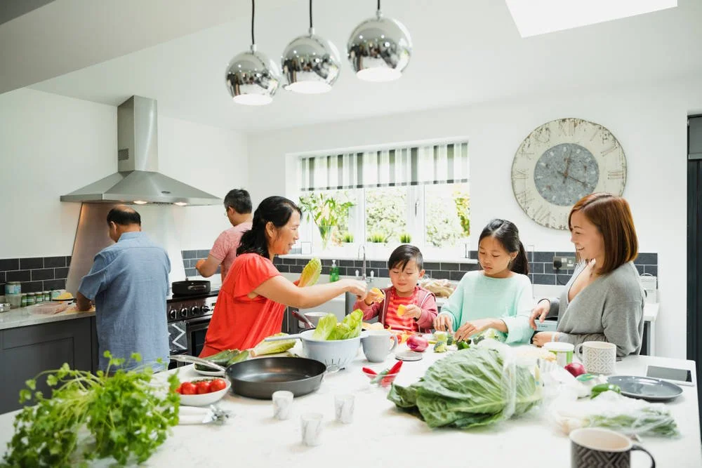 3 generations of family gathered around kitchen island preparing a meal
