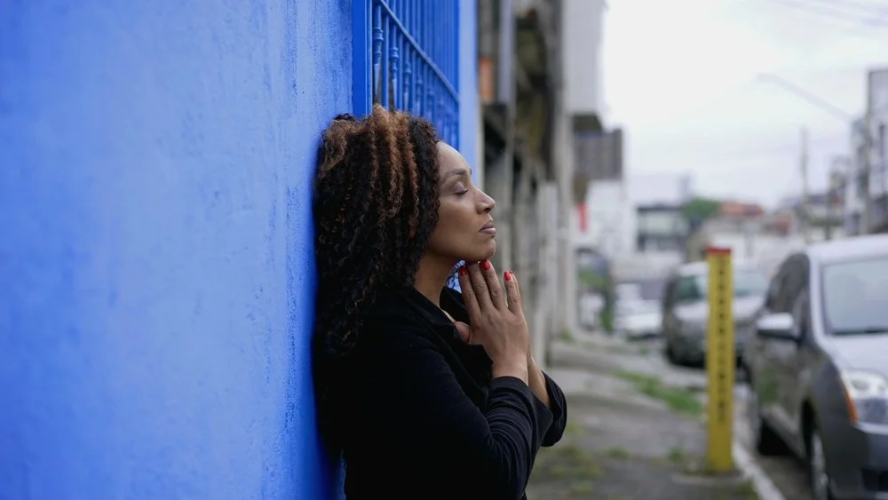 woman with her back against the wall in a posture of surrender while praying