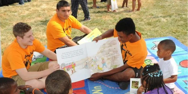 (L-R) Zane Kruszynski, Rudy Vasquez and Jason Johnson share a book with young kids at the Weiler Homes.