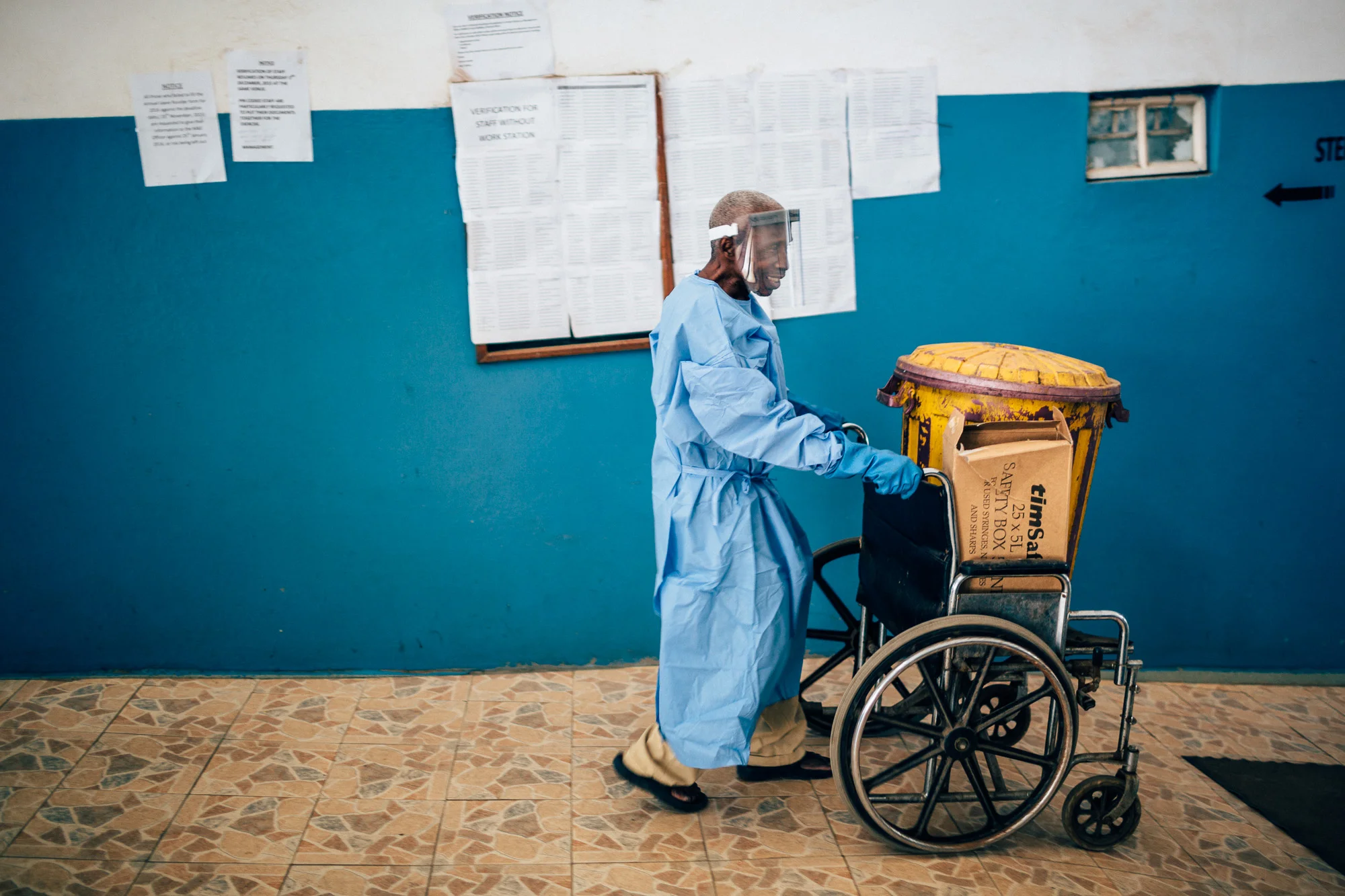 A man pushing a wheelchare with a bin of biologial wase at the OLA During Childrens Hospital, GAVI Alliance. Comic Relief has funded GAVI since 2012 and awared funds in 2014 to purchace and deliver three lifesaving Vaccines to hundres of thousands of children in a selected number of African countries. Immunisation is one of the most effective ways of preventing children from dying from diseses. In africa alone, 600,000 children each year could be saved in vacccine programmes were fully implemened. Most countries have now introduced immunisation programmes in their national health plans, but almost a quater of african children are stil not being vaccinated adequately.