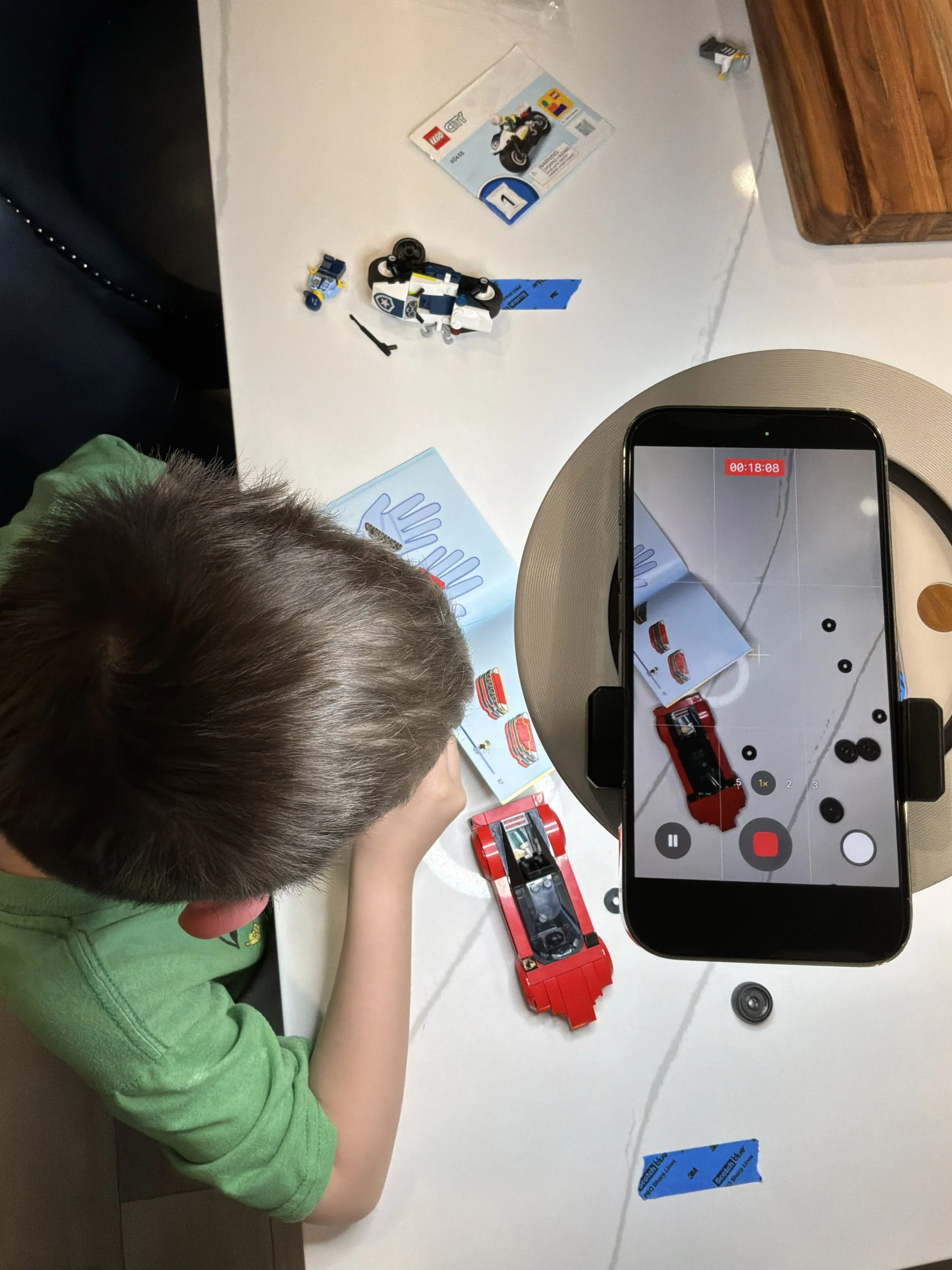child filming a LEGO project using a smartphone mounted under a light