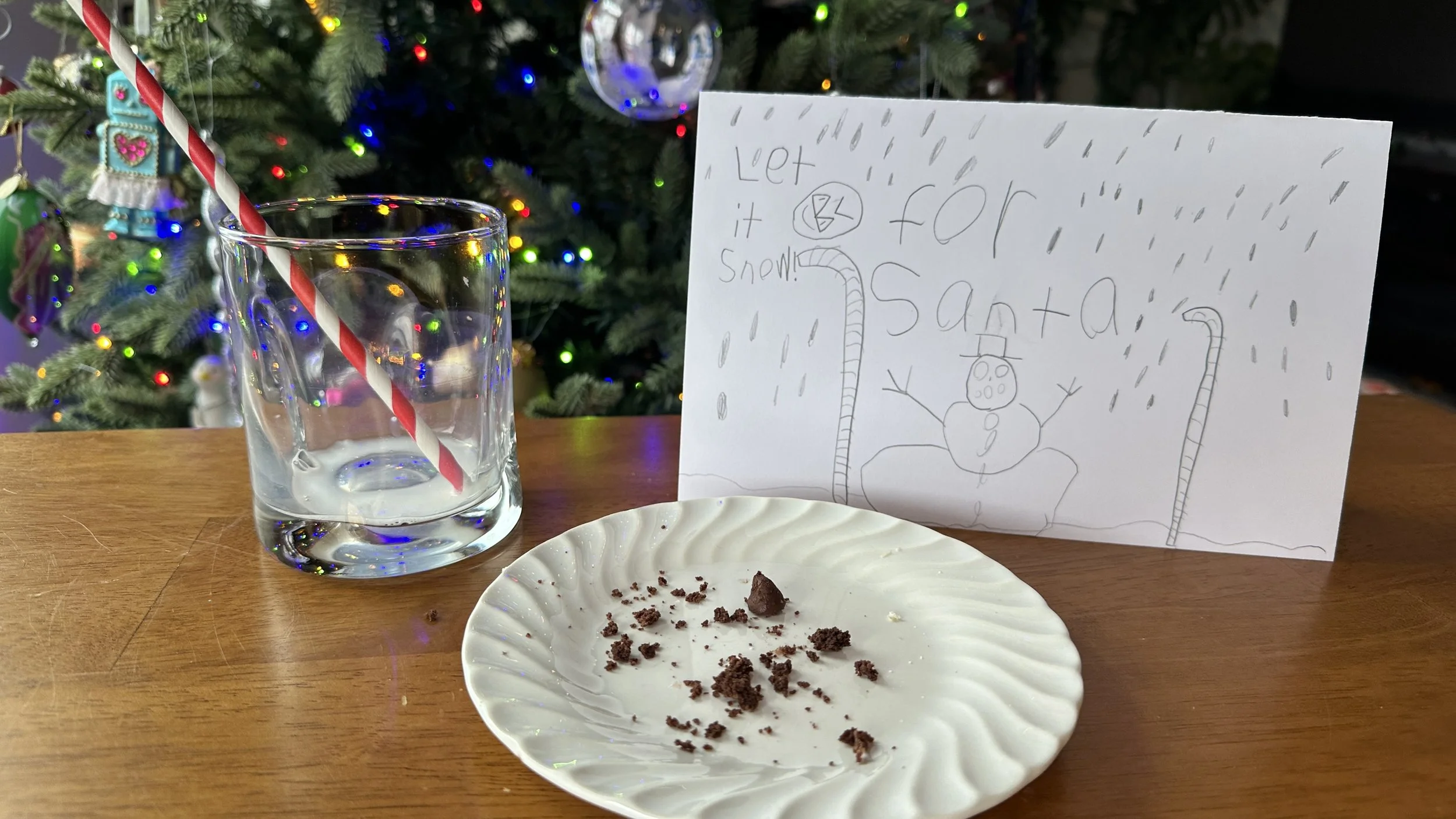 An empty plate with cookie crumbs beside a glass of milk and a handwritten note for Santa, suggesting the cookies were eaten.