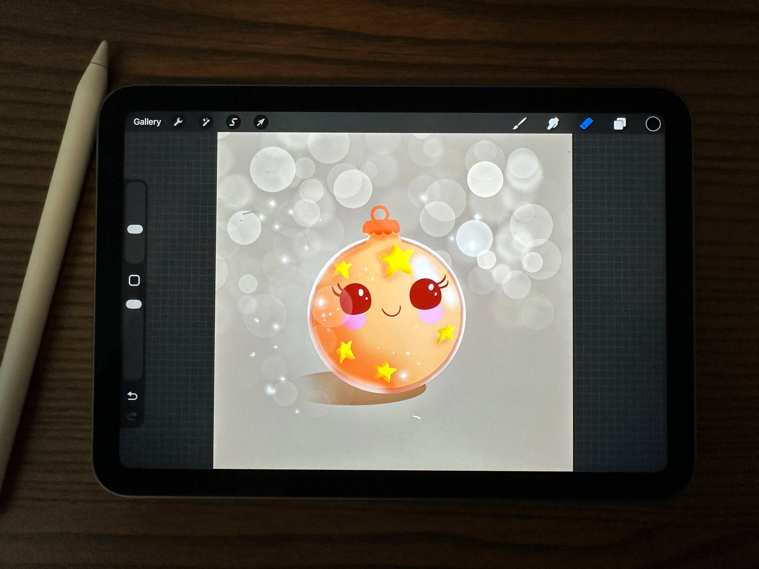 iPad on a wooden table showing a cute ornament character illustration in Procreate, with an Apple Pencil resting nearby.