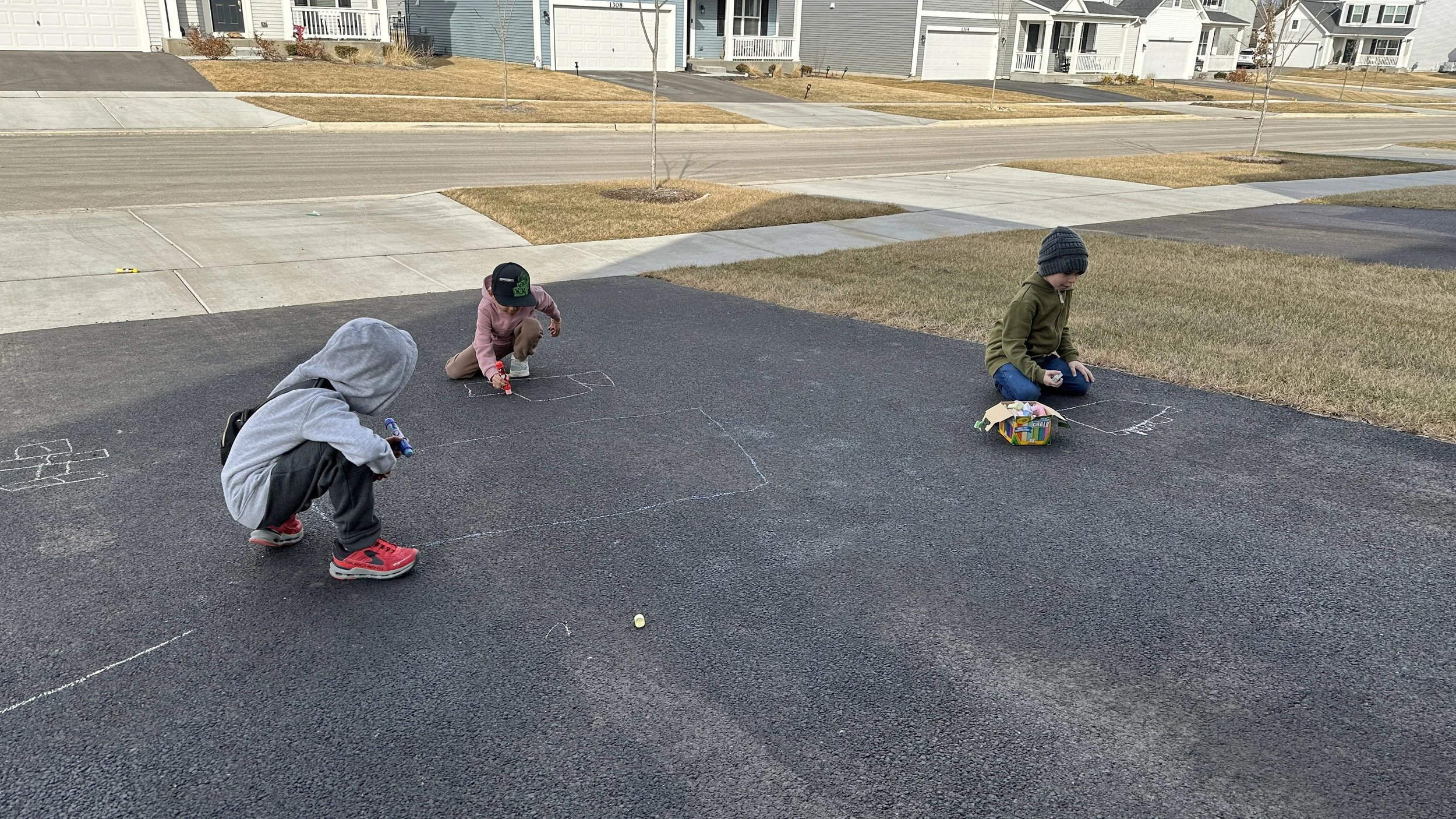 Kids sidewalk chalk drawings on suburban driveway in early spring