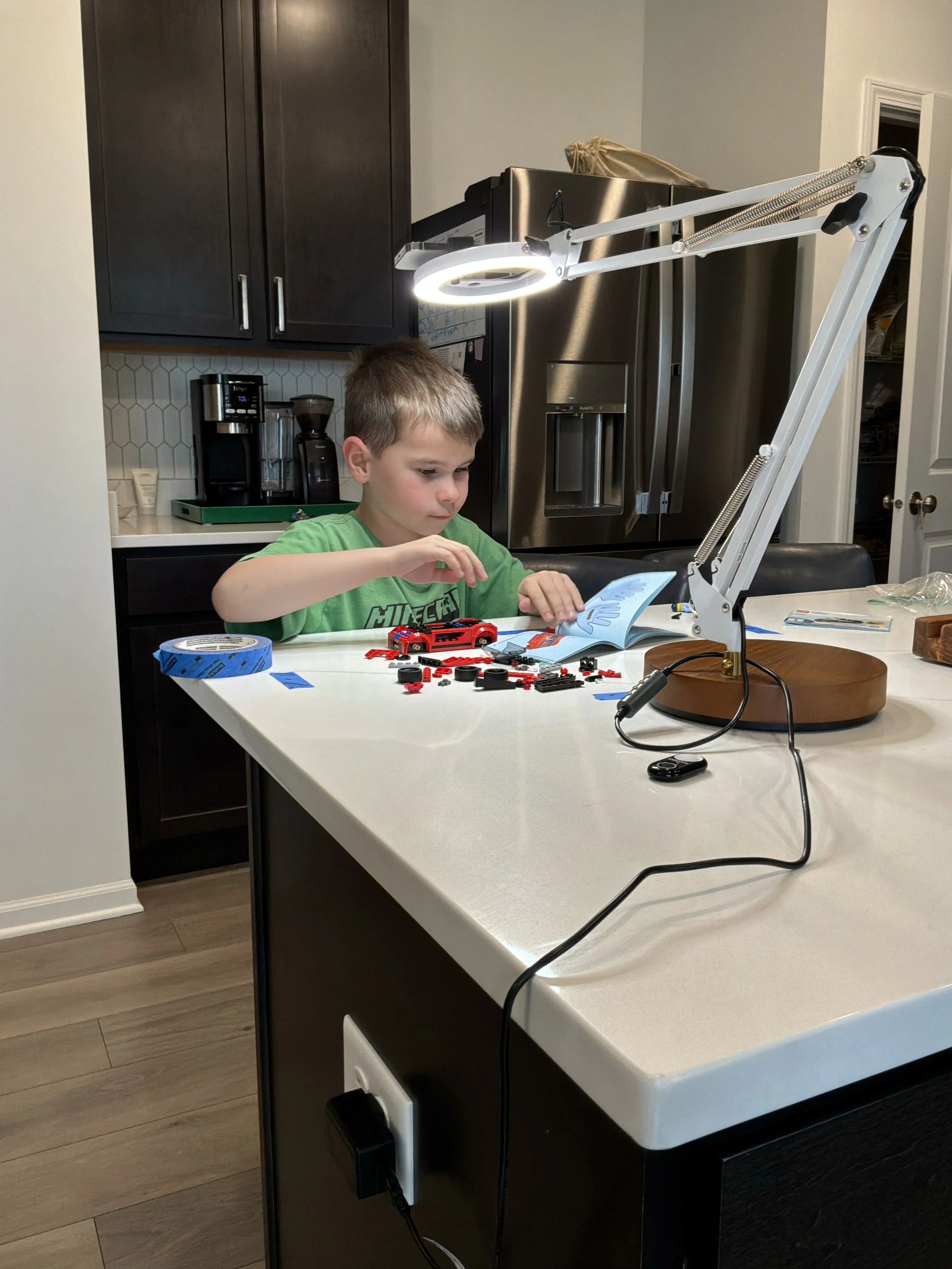 child building LEGO car at kitchen counter under filming lamp