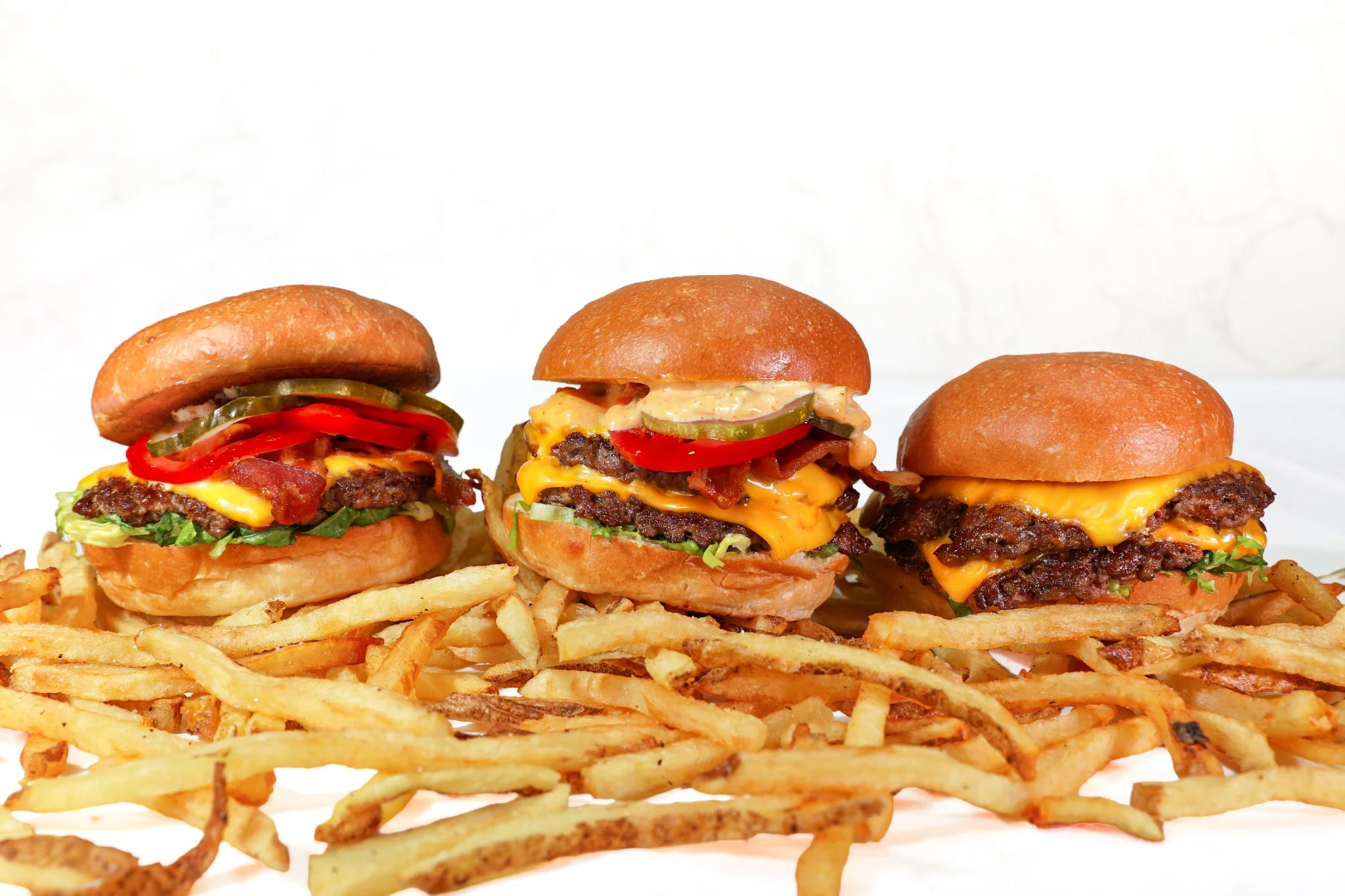 Restaurant food photography of three handcrafted burgers with French fries arranged for menu and marketing materials.