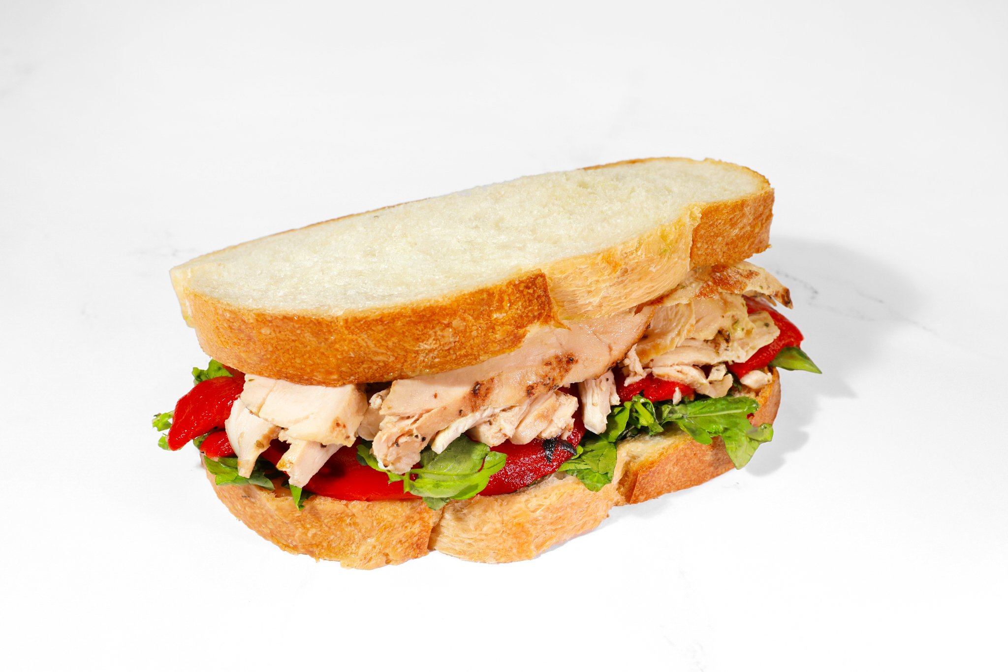 Commercial food photography of a grilled chicken club sandwich with bacon, lettuce, tomato, and toasted bread.