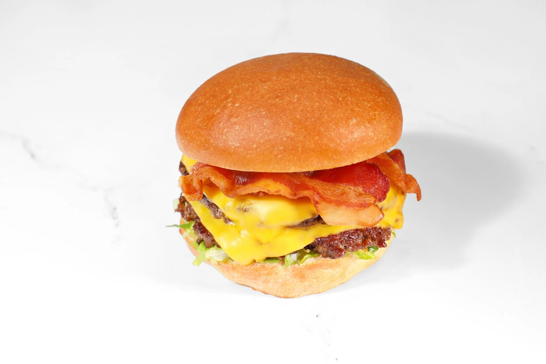 Commercial food photography of a bacon cheeseburger with melted cheese, crisp bacon, lettuce, tomato, and a toasted bun.