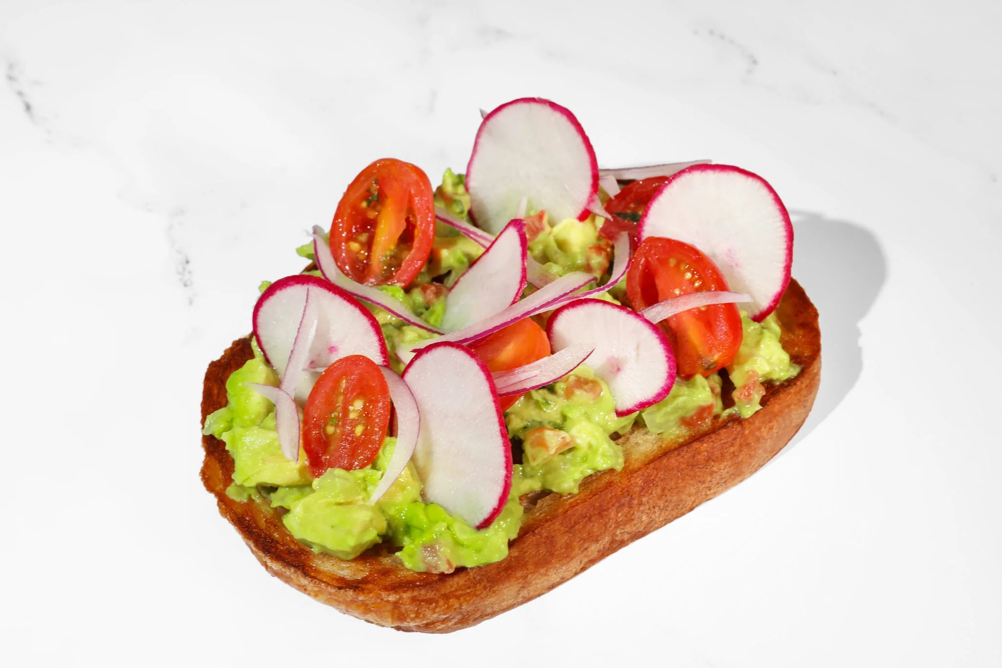 Commercial food photography of avocado toast topped with fresh herbs, tomatoes, and seasoning for a restaurant menu.