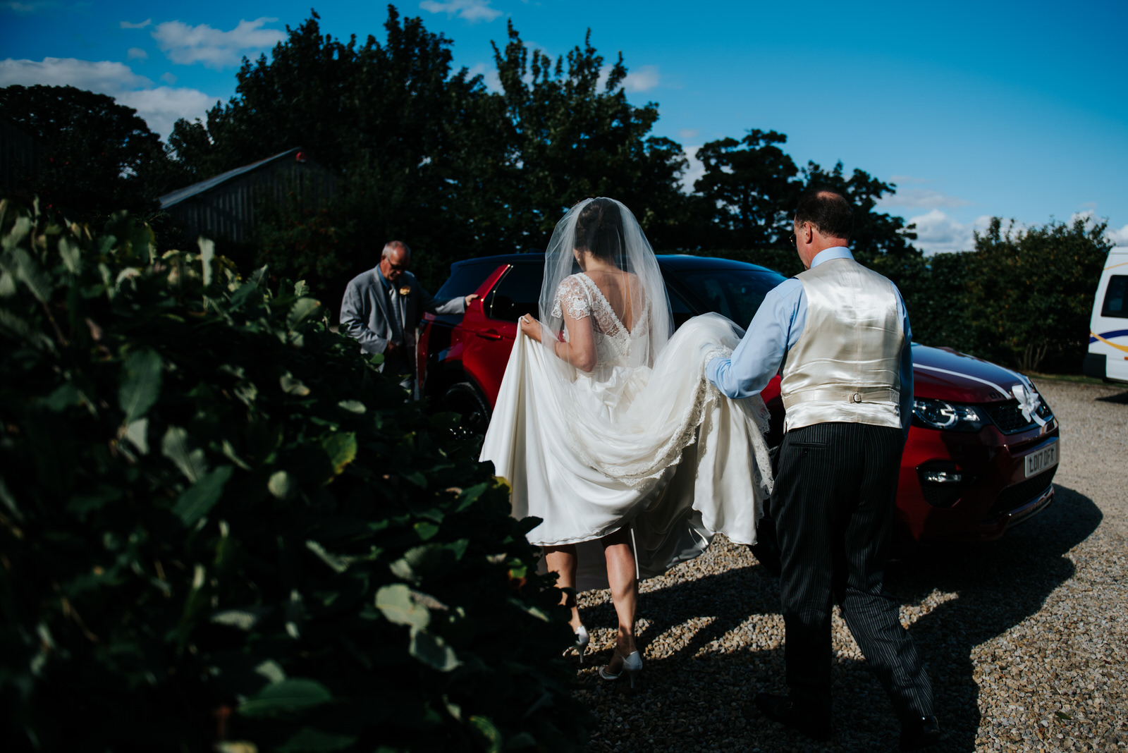 Father of the bride and bride walk towards car which will take t