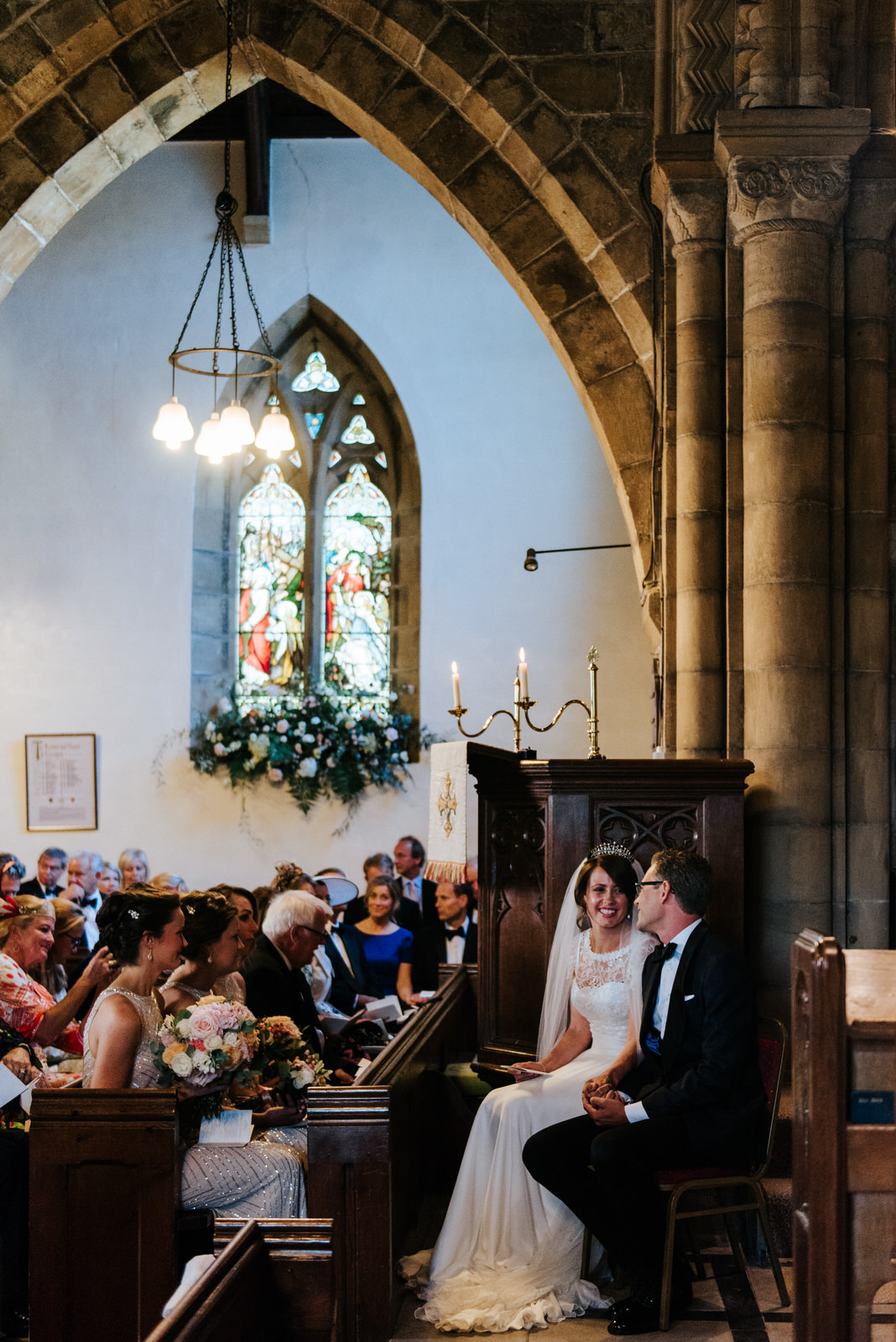 Bride and groom sat down smiling at each other in Church ceremon