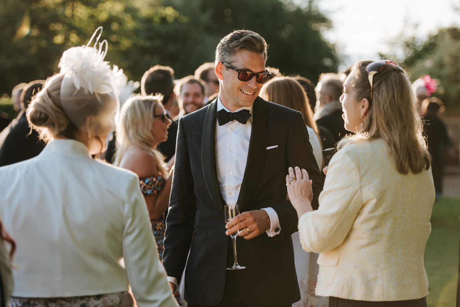 Groom drinking champagne and talking to guests outside the marqu