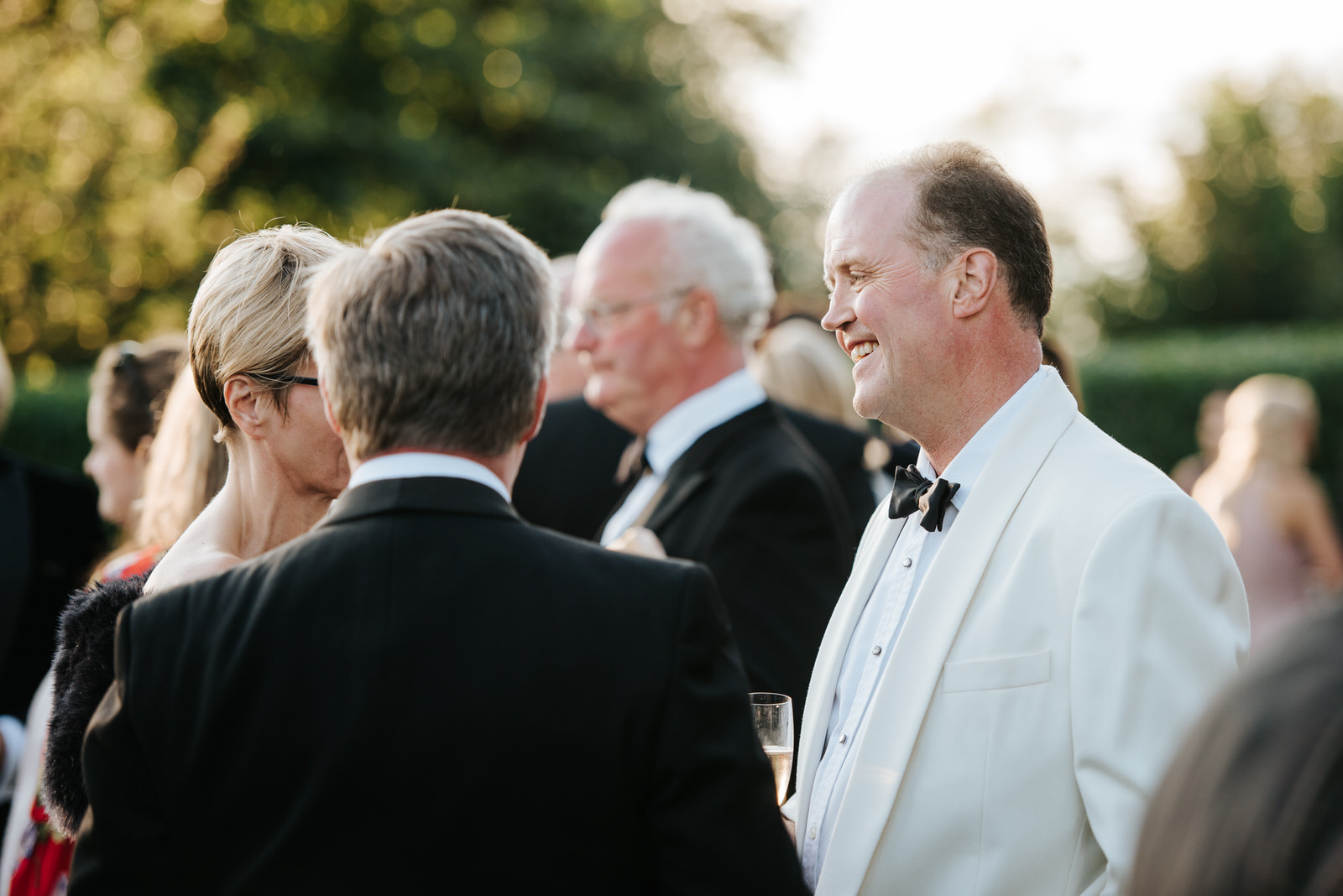 Father of the Bride talks to guests in sun-drenched garden durin