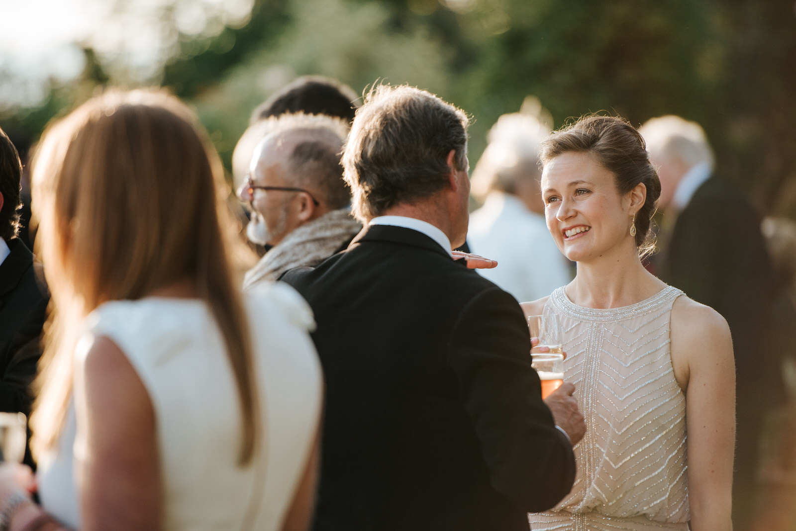 Sister of the Bride smiles in garden as she talks to guests duri