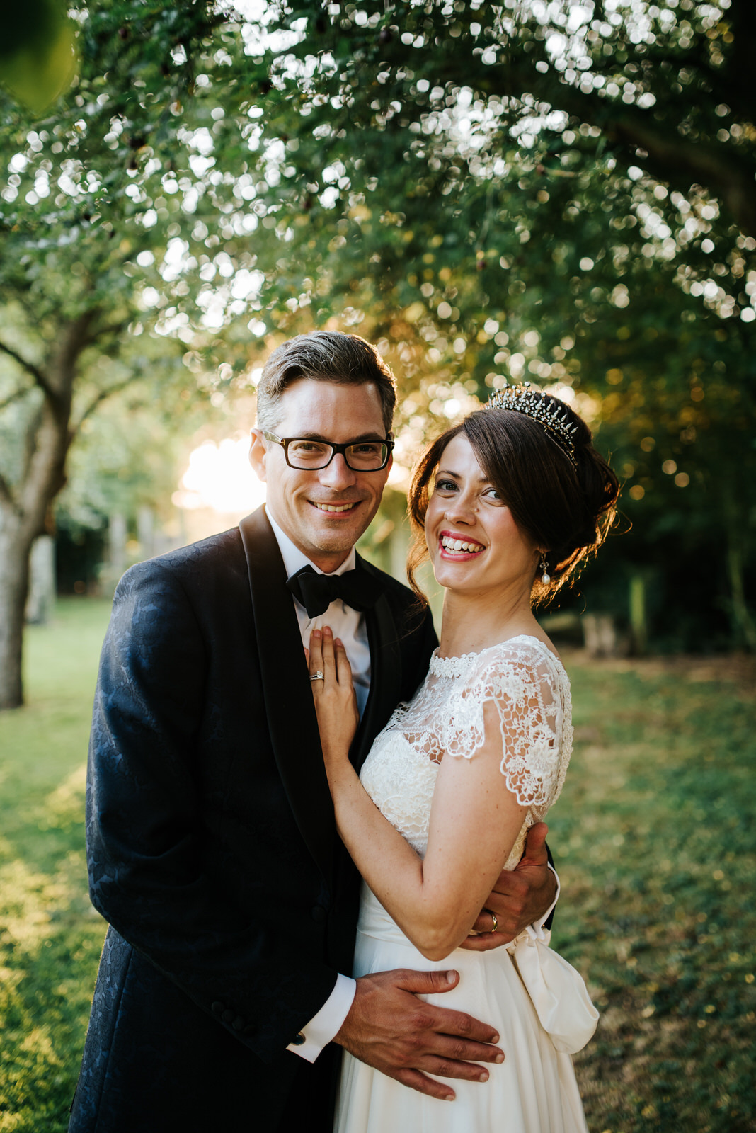 Bride and Groom look into camera as they stand in orchard