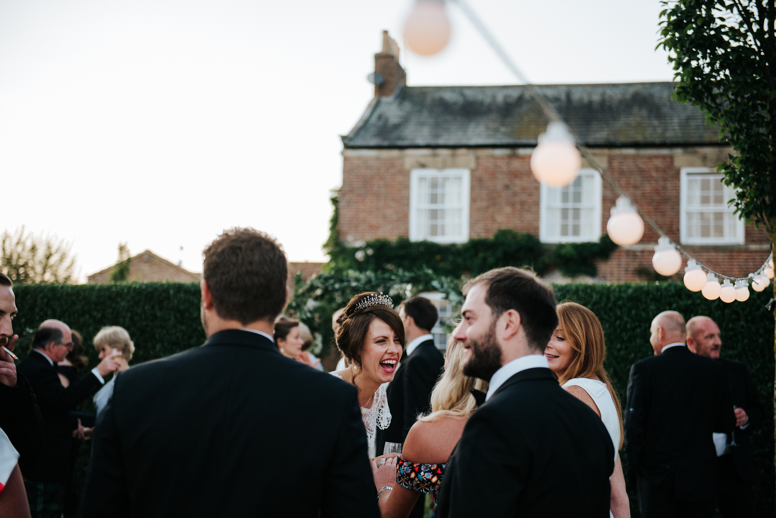 Bride laughs loudly in front of house as wedding reception ends