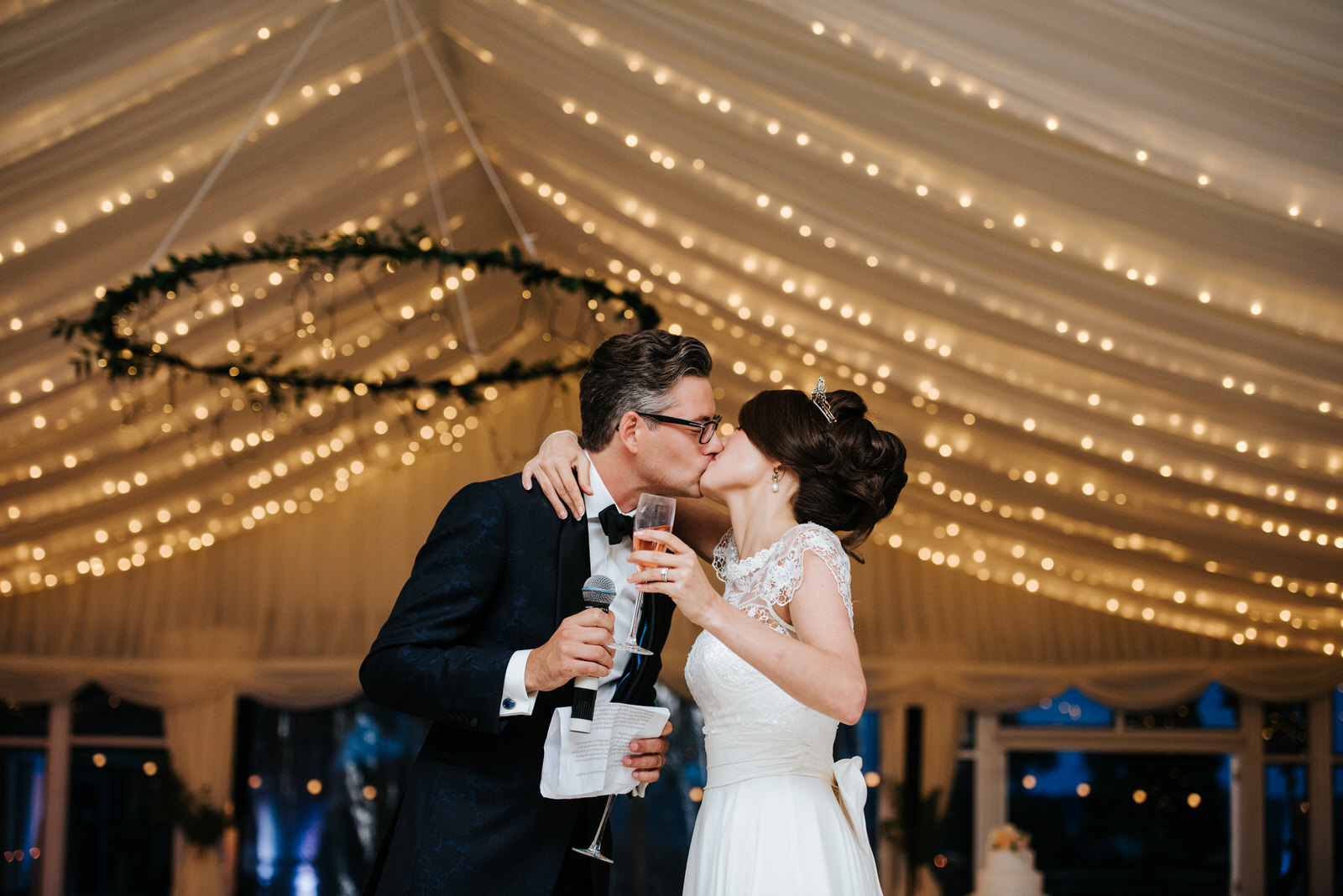 Bride and groom kiss romantically under Marquee fairy lights