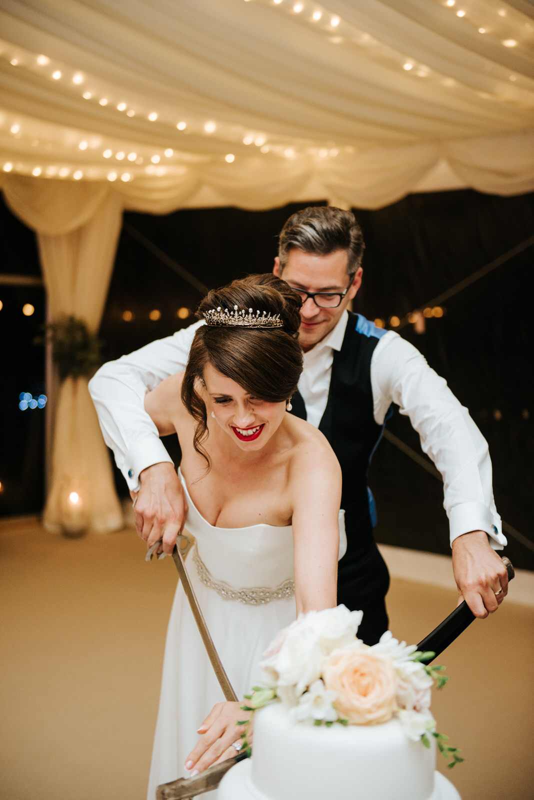 Bride and Groom lean in to cut the wedding cake with military sw